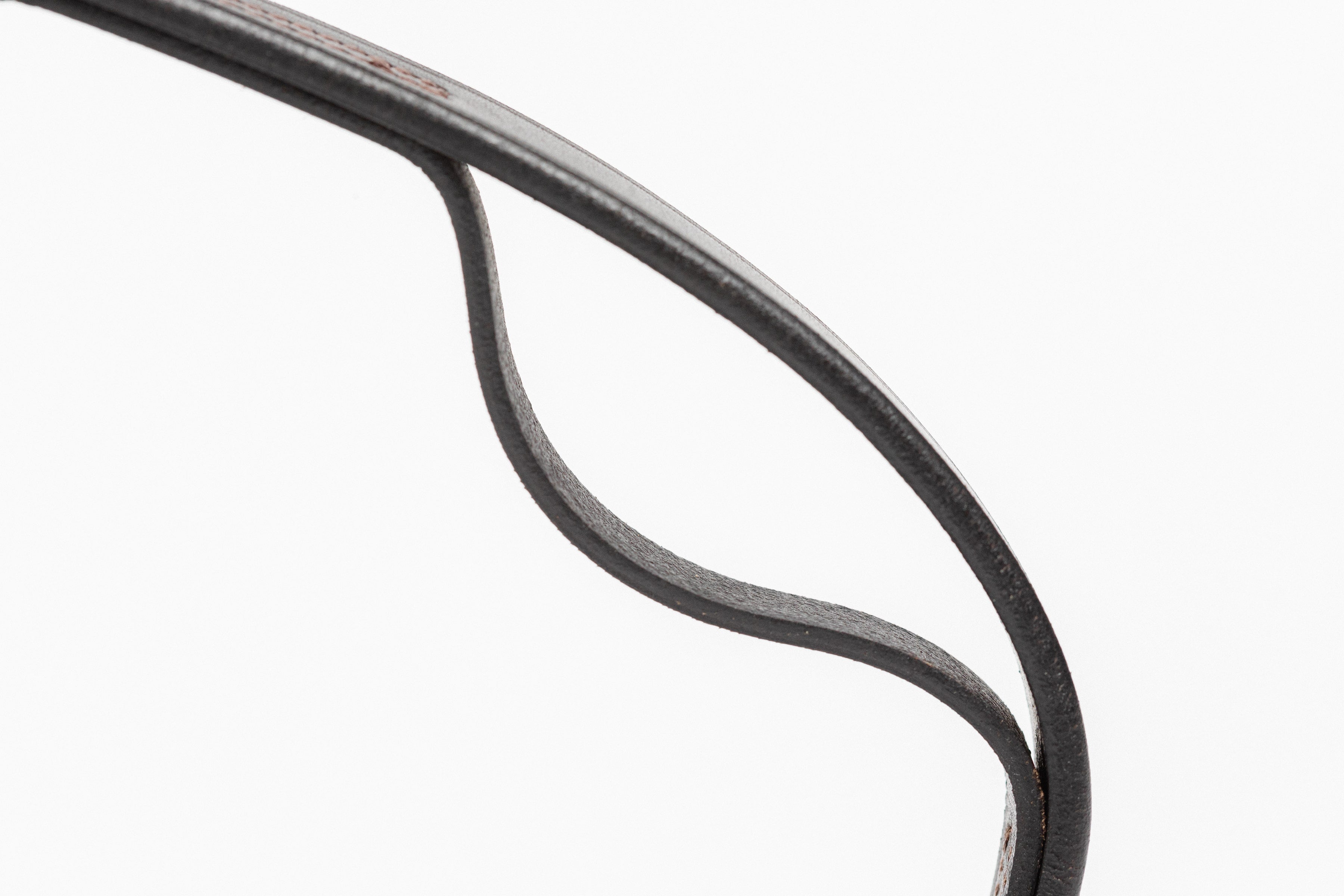 Detail of a high-quality black leather strap, highlighting the supple texture and precise edge finishing, suitable for equestrian or leather goods context.
