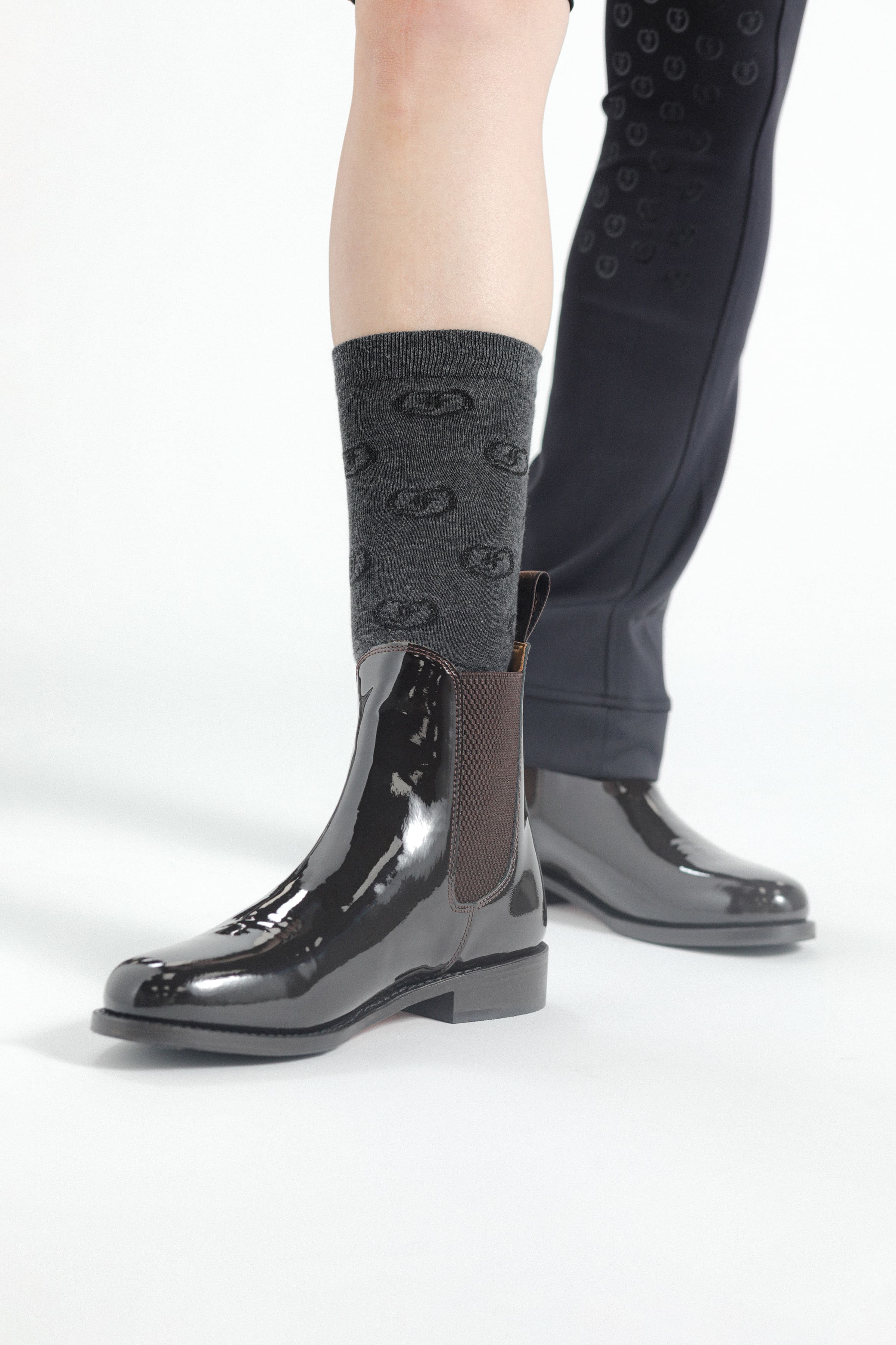 Single black patent leather Adelaide Show Jodhpur Boot on a person's foot, with patterned socks visible