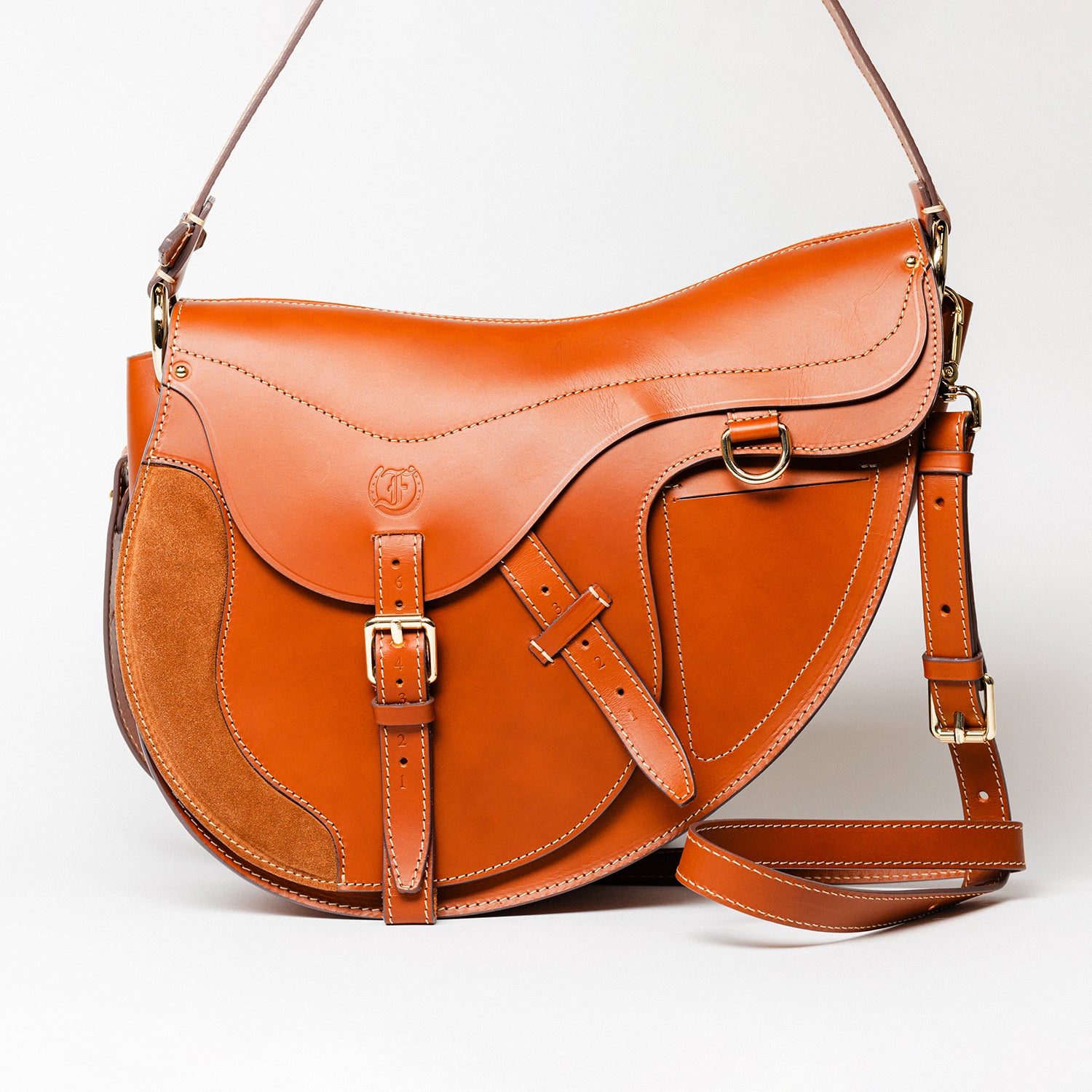 Freedman’s Burghley Shoulder Bag in cognac leather, featuring gold finished hardware, a distinctive saddle-inspired silhouette, and an adjustable shoulder strap, on a white background.