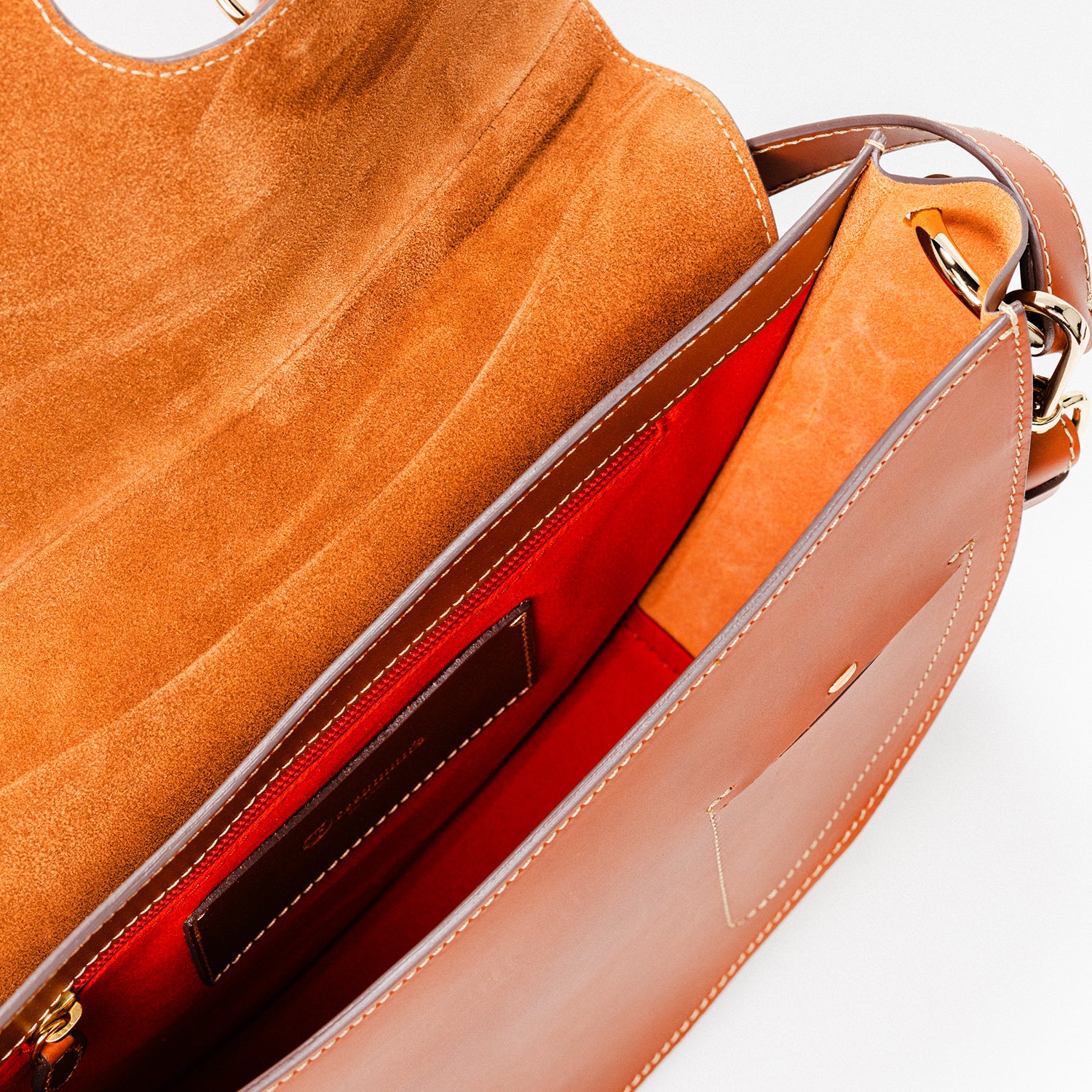 Freedman’s Burghley Shoulder Bag in cognac leather, featuring gold-tone hardware, organized interior with multiple compartments and a bright red lining, and an adjustable shoulder strap, shown with the flap open on a white background.
