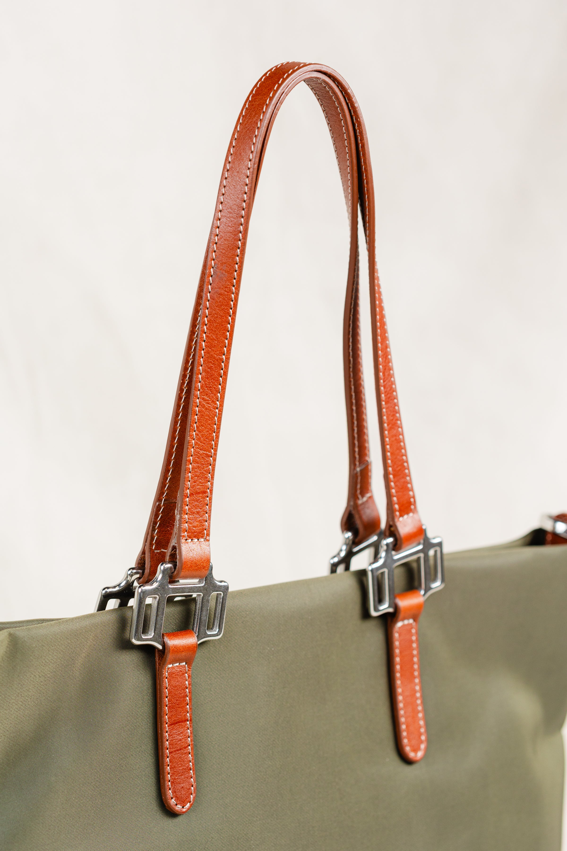 Conestoga Tote by Freedman's, close-up shot of the brown leather handles showing detailed stitching and silver hardware connectors on the olive green bag.