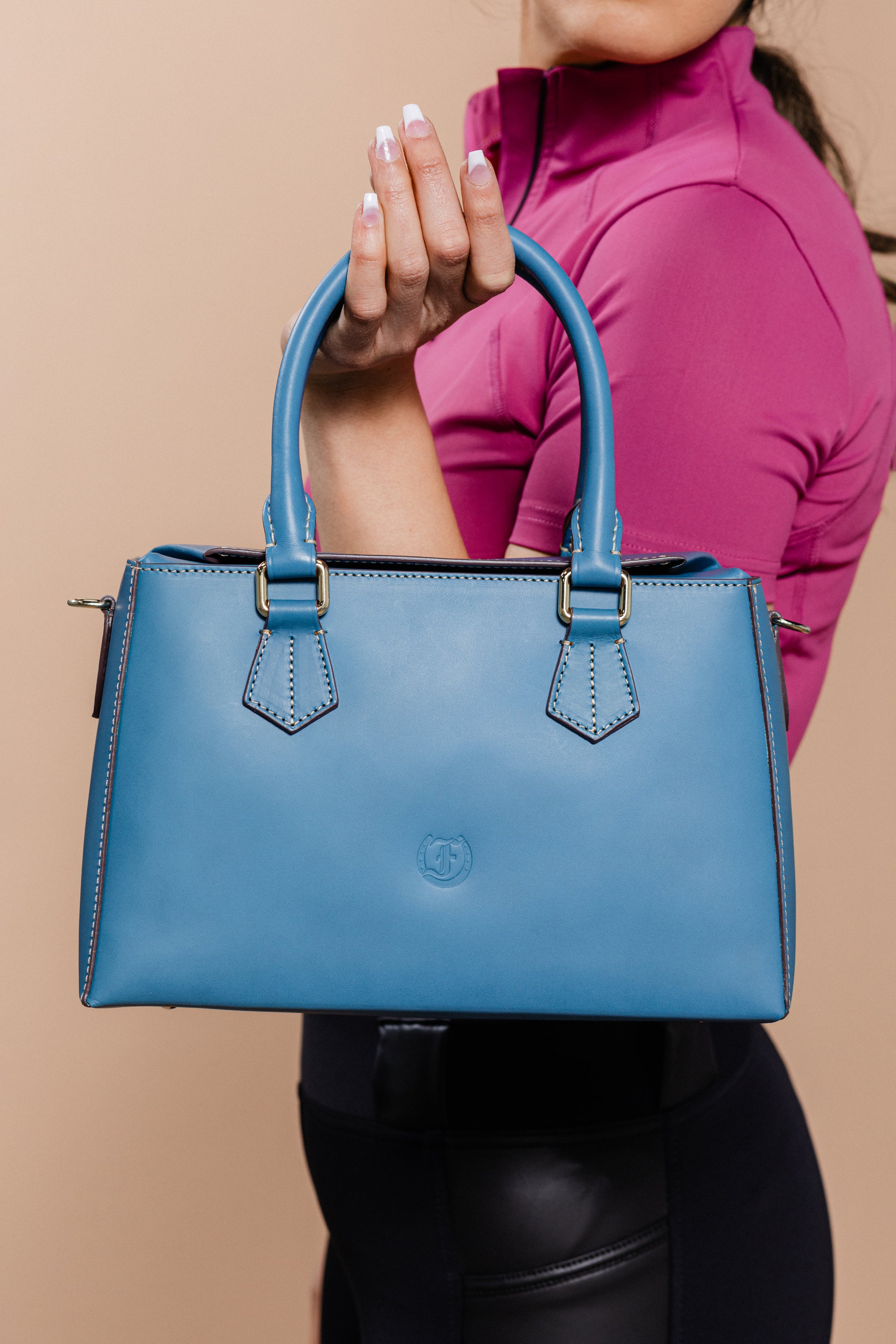 Stylish blue Dormeuse Bag, a luxury leather handbag, elegantly carried with a chic equestrian-inspired outfit. Perfect blend of fashion and functionality