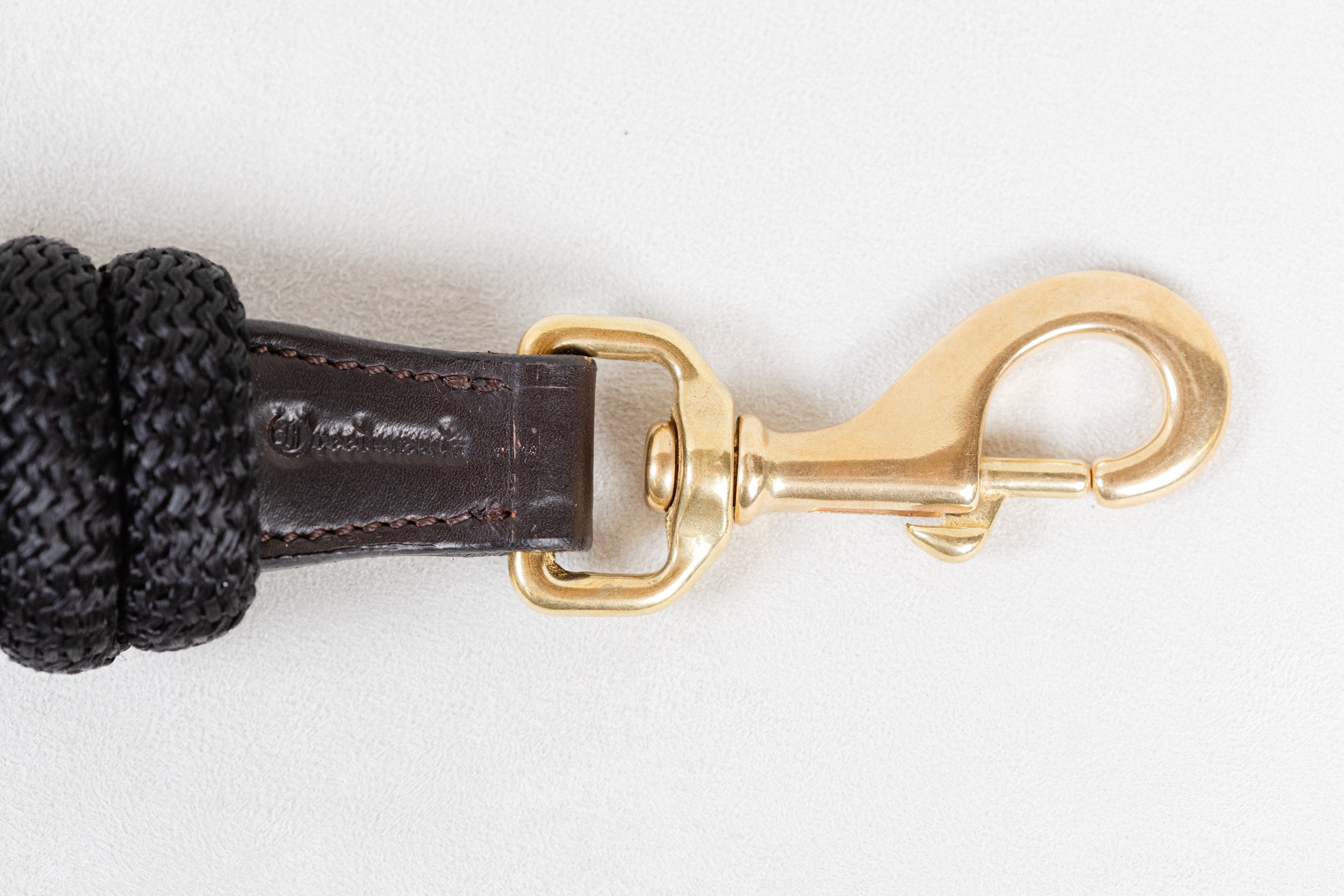 Detailed close-up of the brass snap hook on a Freedman Harness black lead rope, showing the spring-loaded mechanism and the rich texture of the brown leather wrap on a white background