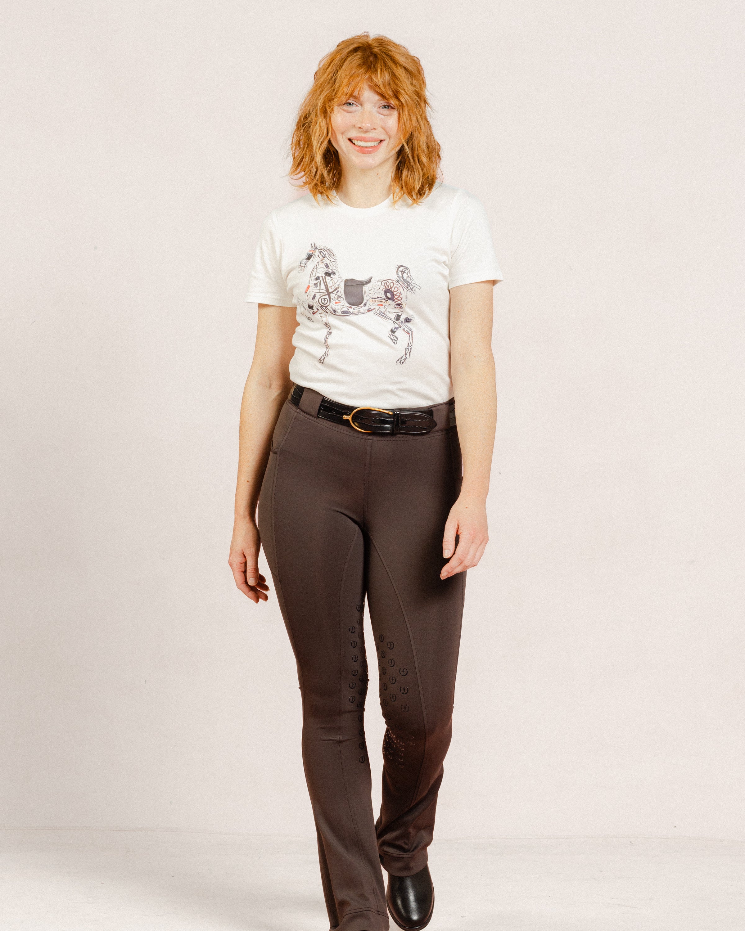 Person wearing a white Signature Ladies' High Stepper T-shirt and After Dark Brown Jods by Freedman’s Harness on a plain background.