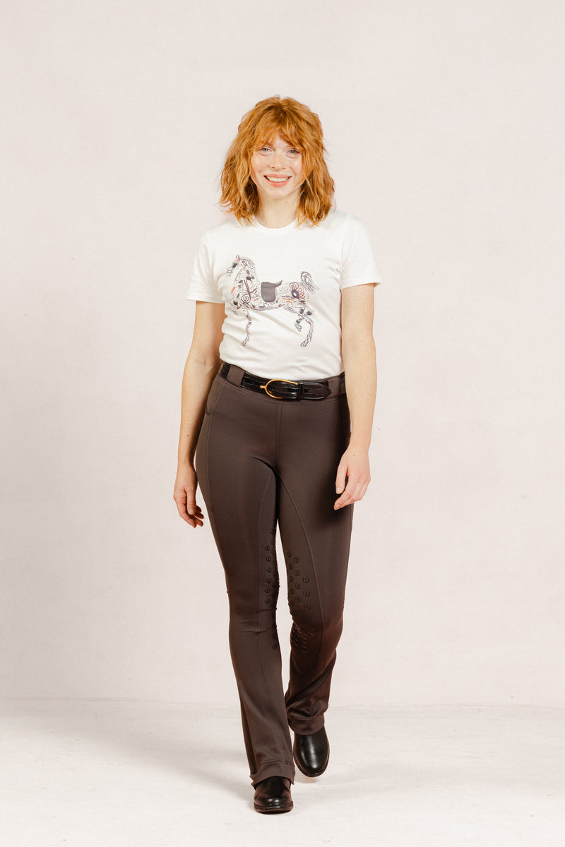 Person wearing a white Signature Ladies' High Stepper T-shirt and After Dark Brown Jods by Freedman’s Harness on a plain background.