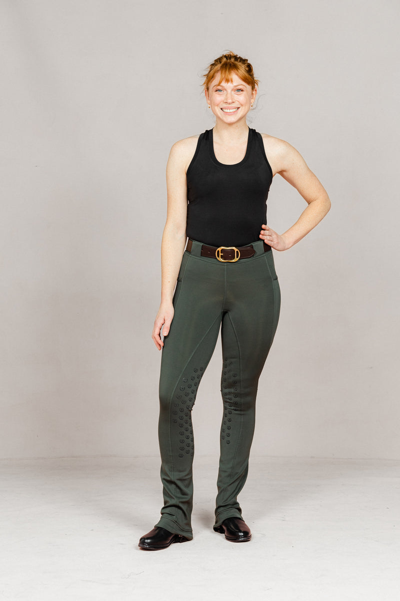 Woman wearing Umber Green jodhpurs by Freedman Harness with full seat grip, brown leather belt, and black riding boots – stylish equestrian outfit for everyday riding