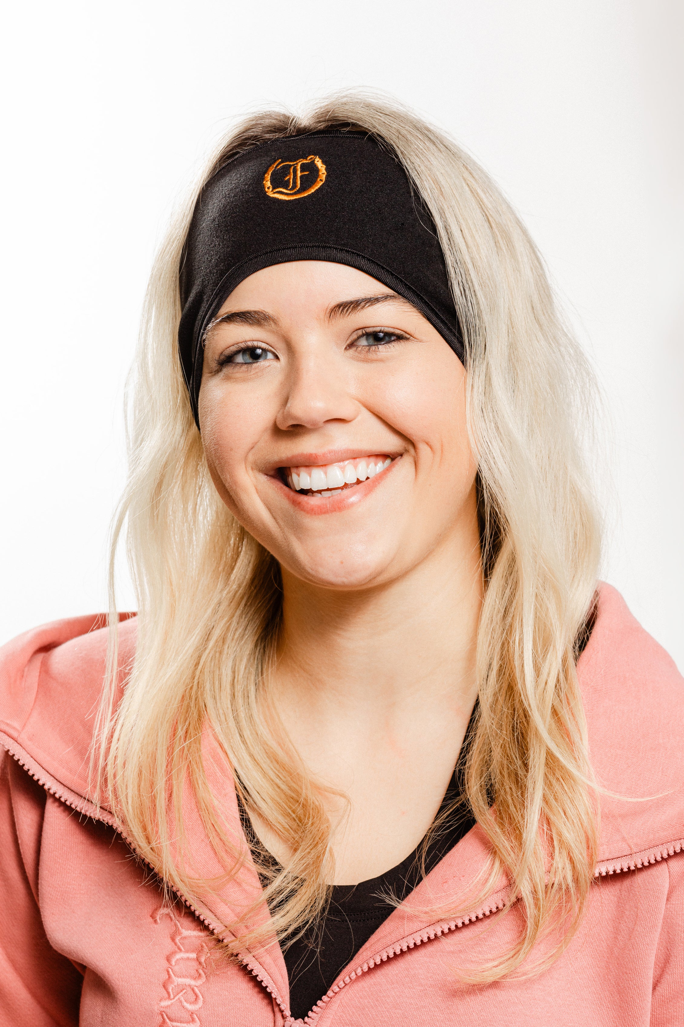 A close up of a woman wearing the Freedman's Fleece Headband with Embroidered Freedman’s “F”  Logo with a Pink Hoodie.