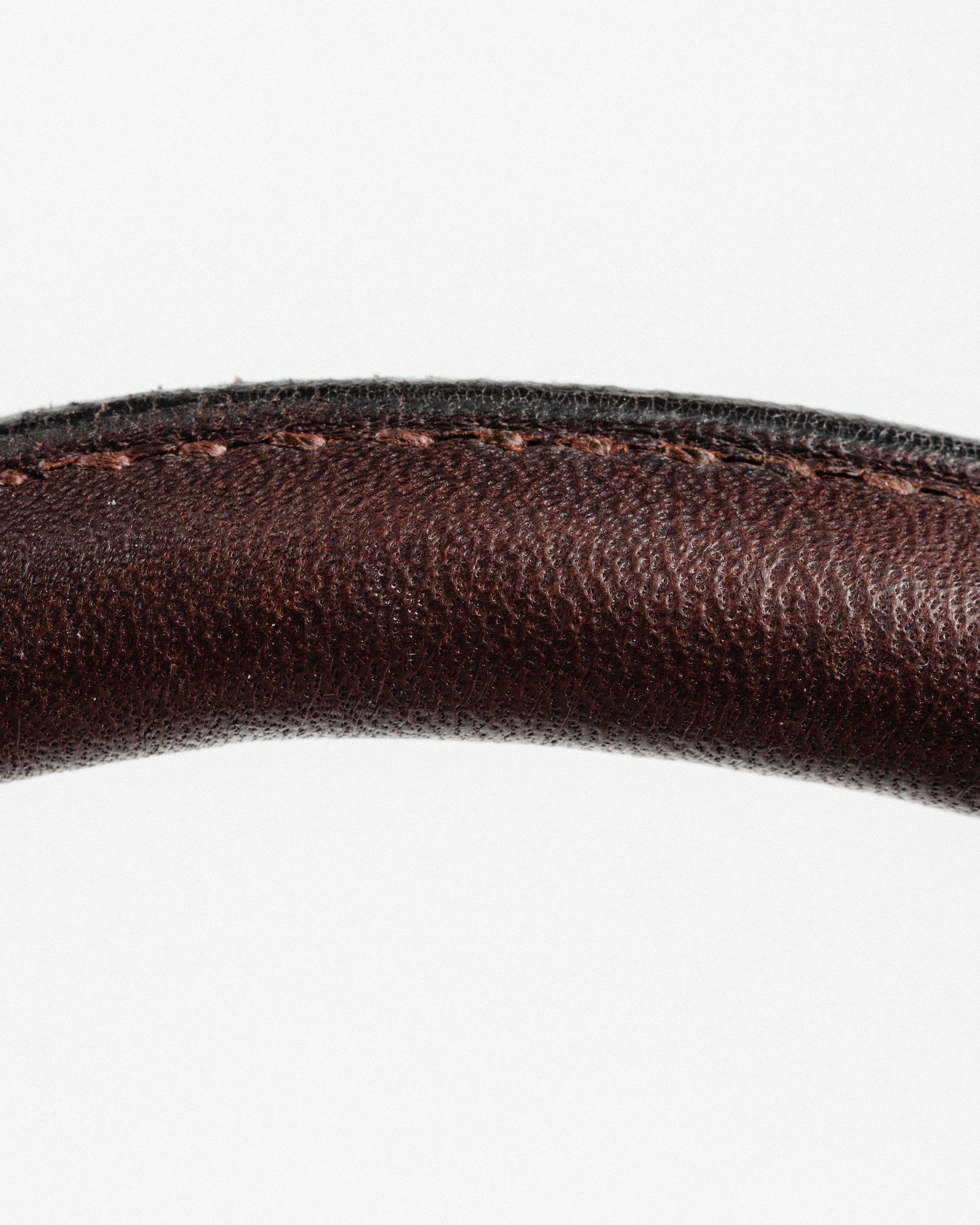 Close-up of curved, dark brown leather, highlighting the detailed stitching along the edge, against a white background.