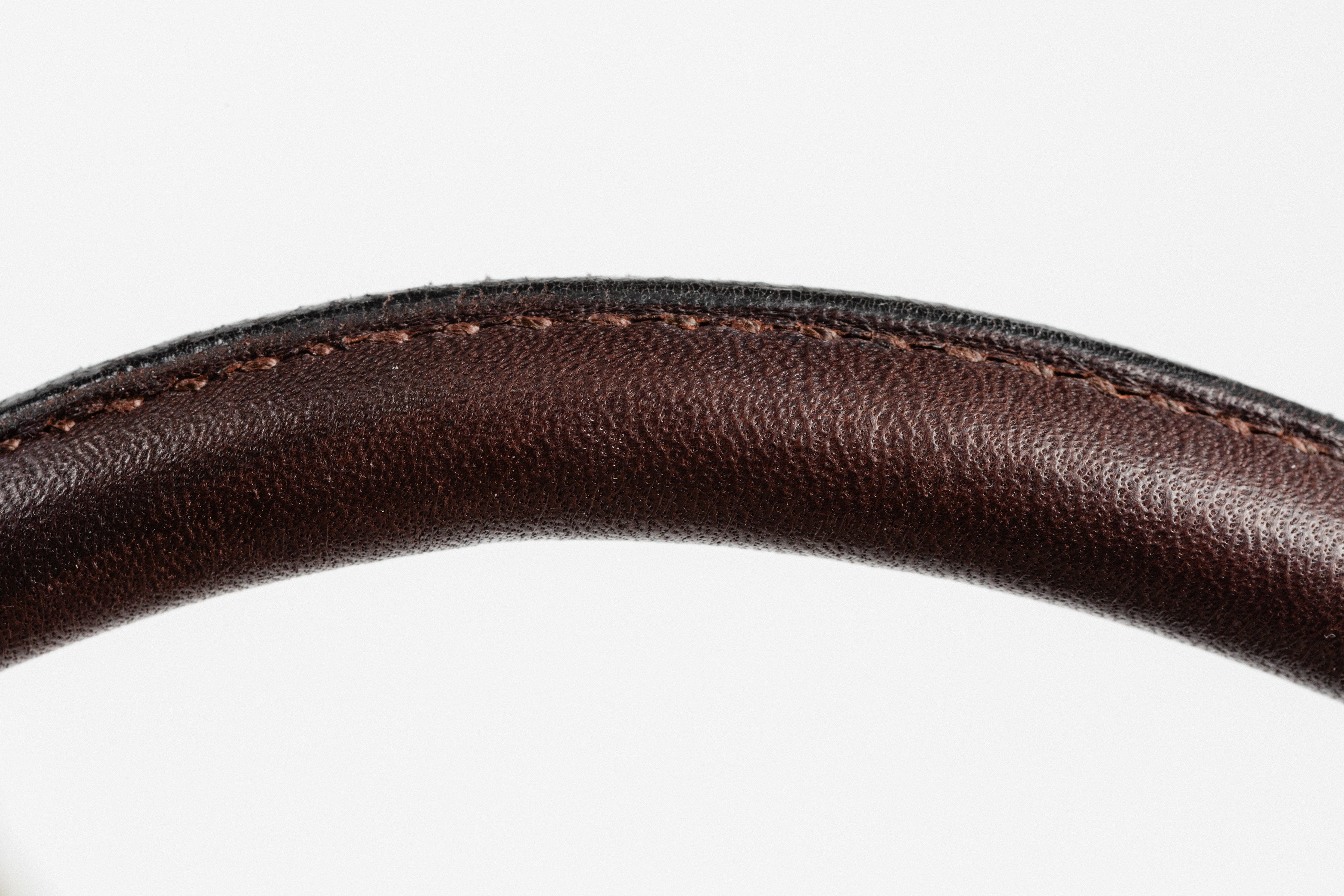 Close-up of curved, dark brown leather, highlighting the detailed stitching along the edge, against a white background.
