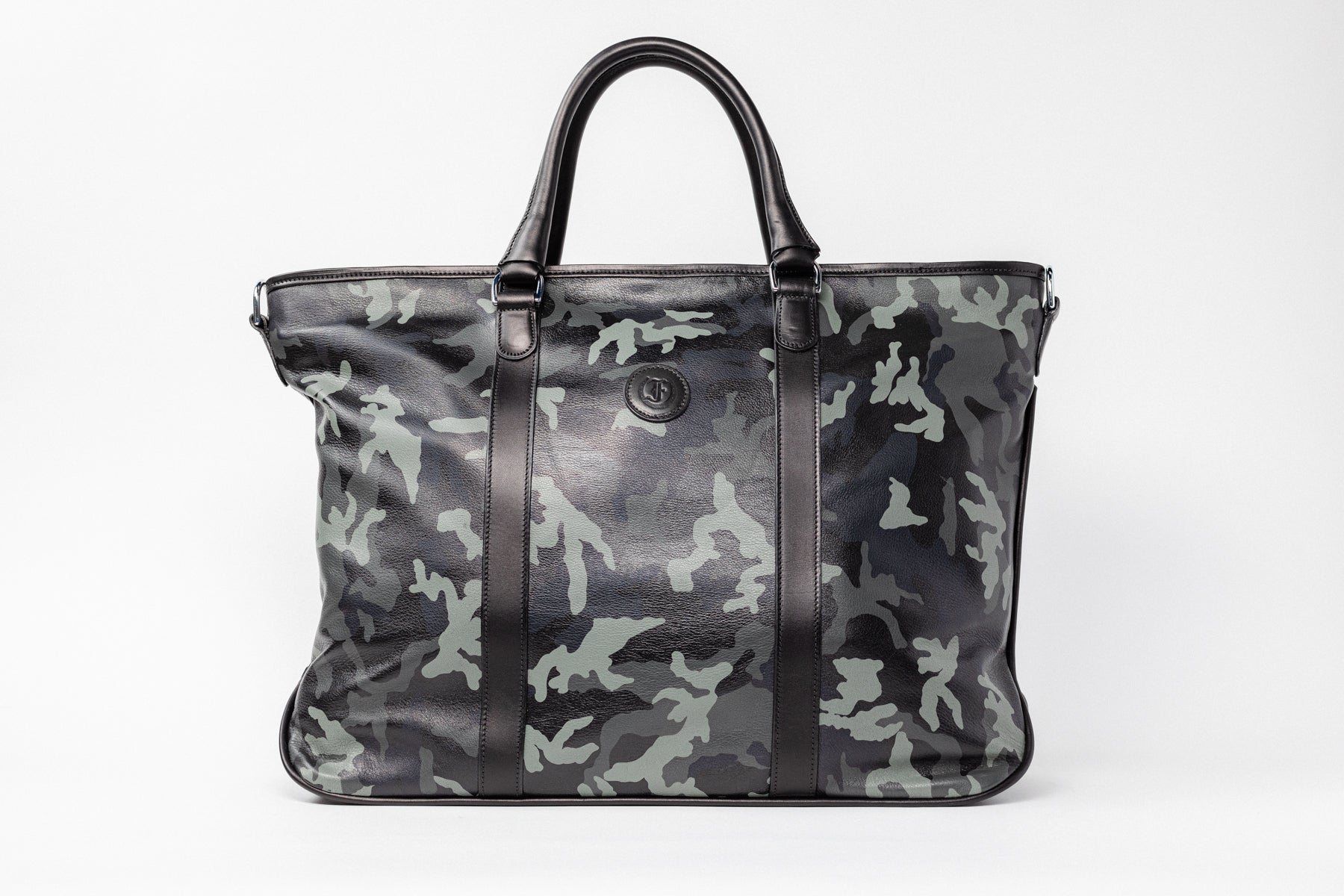 Freedman's Victoria Tote Large, dark textured leather, Camo leather trim along edges and center straps, embossed circular logo on front, light contrast stitching, dual rolled handles with metal hardware, light background.