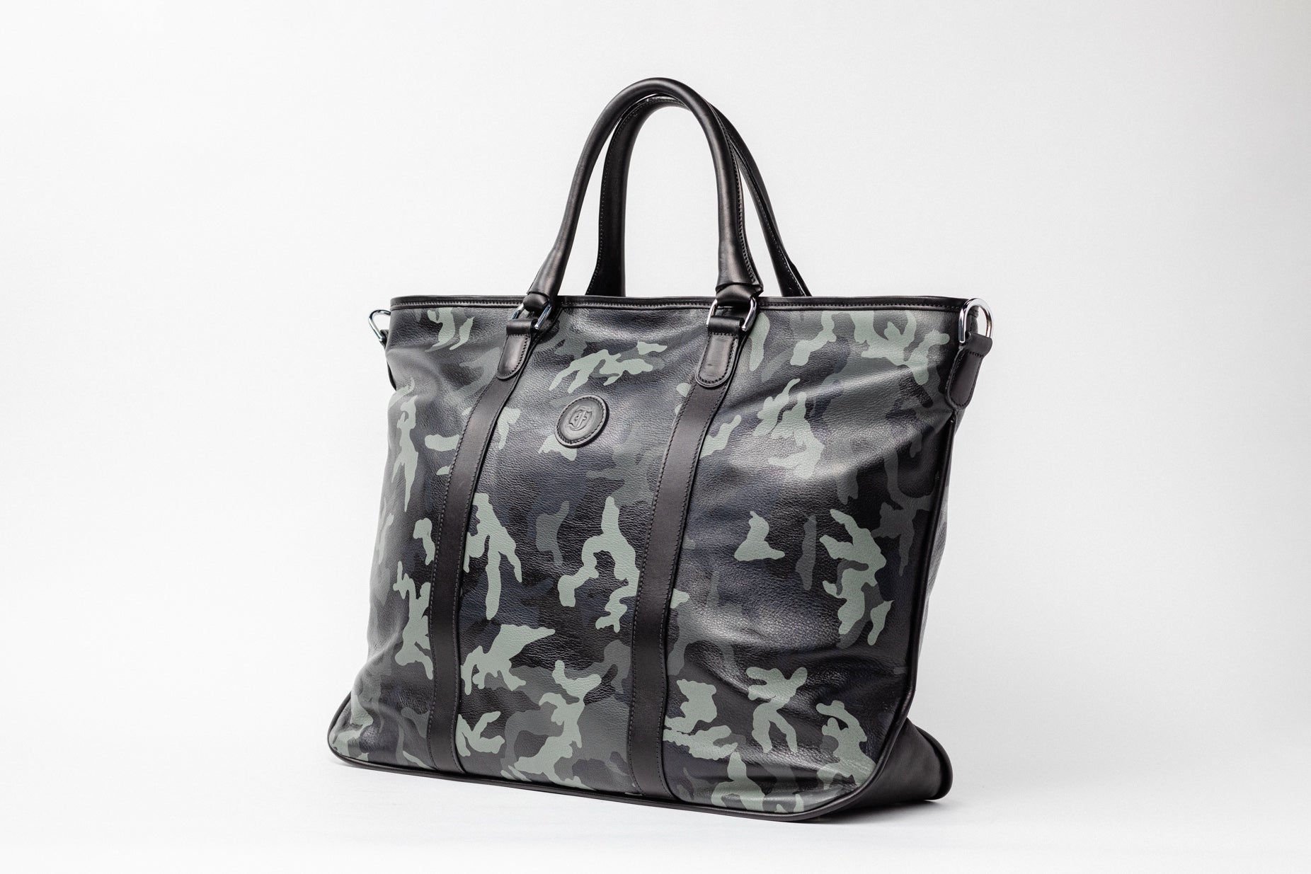 Freedman's Victoria Tote Large, camouflage patterned leather, dark leather trim along edges and center straps, embossed circular logo on front, dual rolled handles, light background.