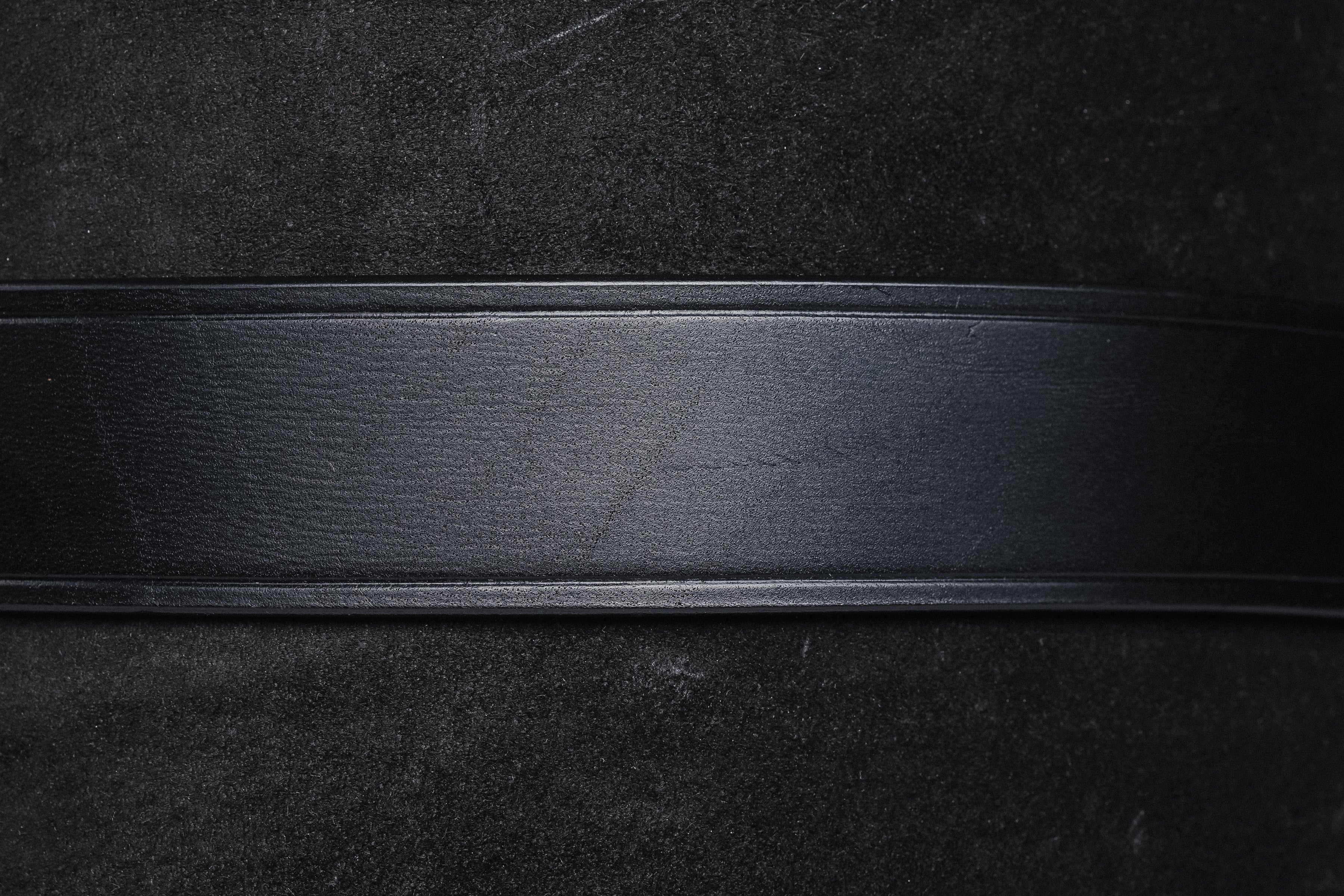 Black leather belt strap, close-up showing texture and construction.