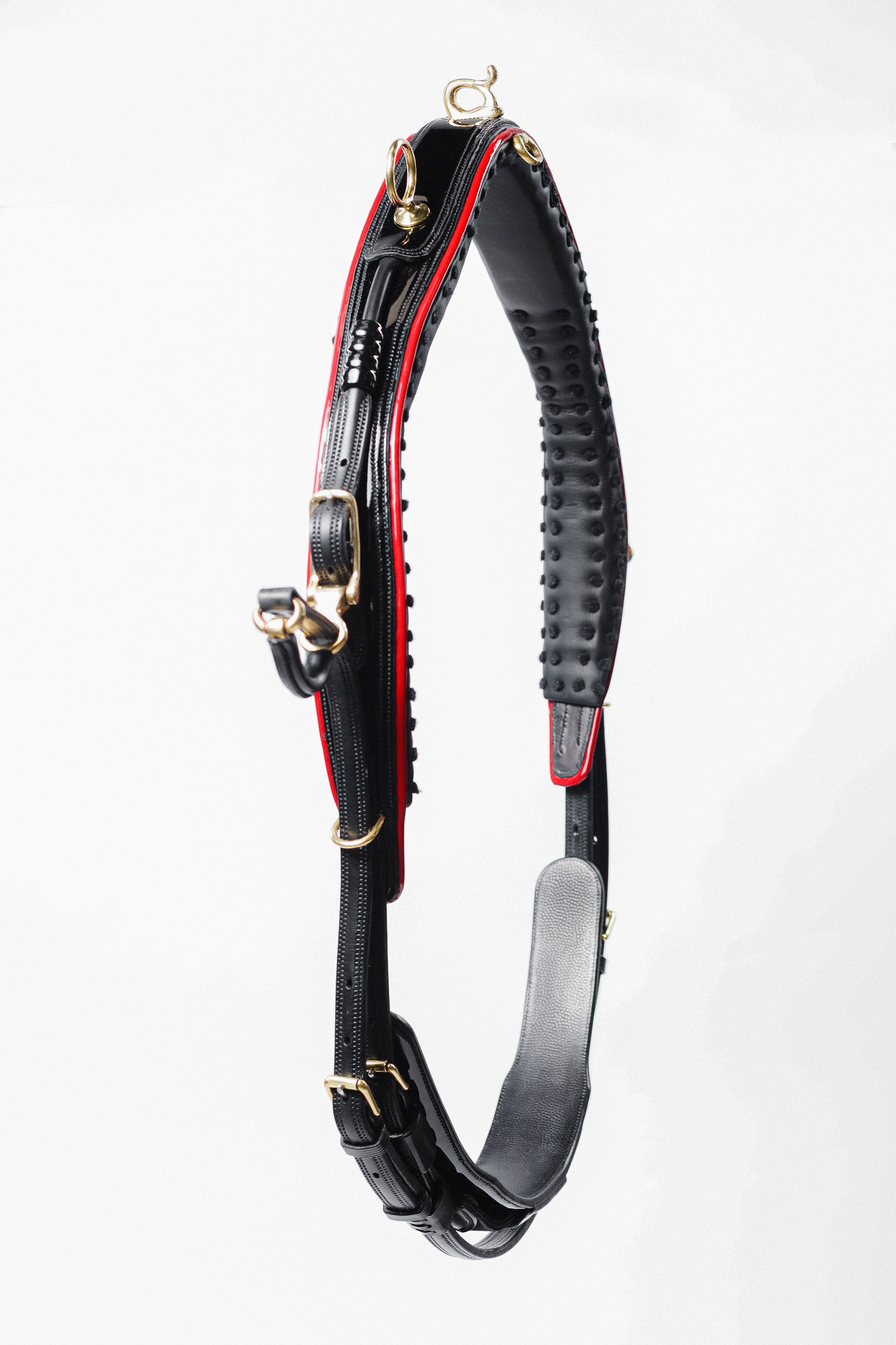 A black leather horse neck strap with red padding and gold buckles, hanging against a white background.