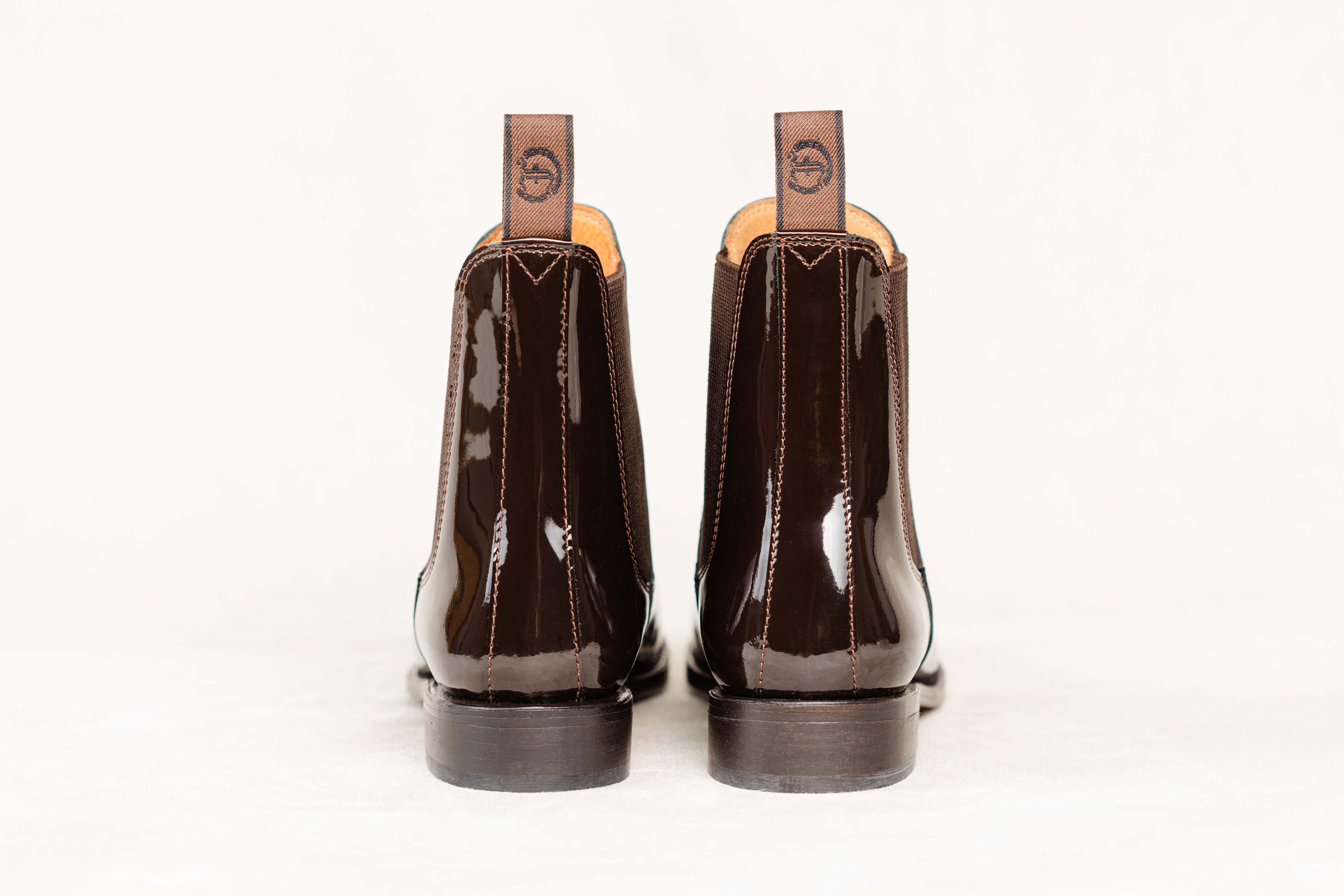 Back view of a pair of brown patent leather Adelaide Show Jodhpur Boots, isolated on a white background.