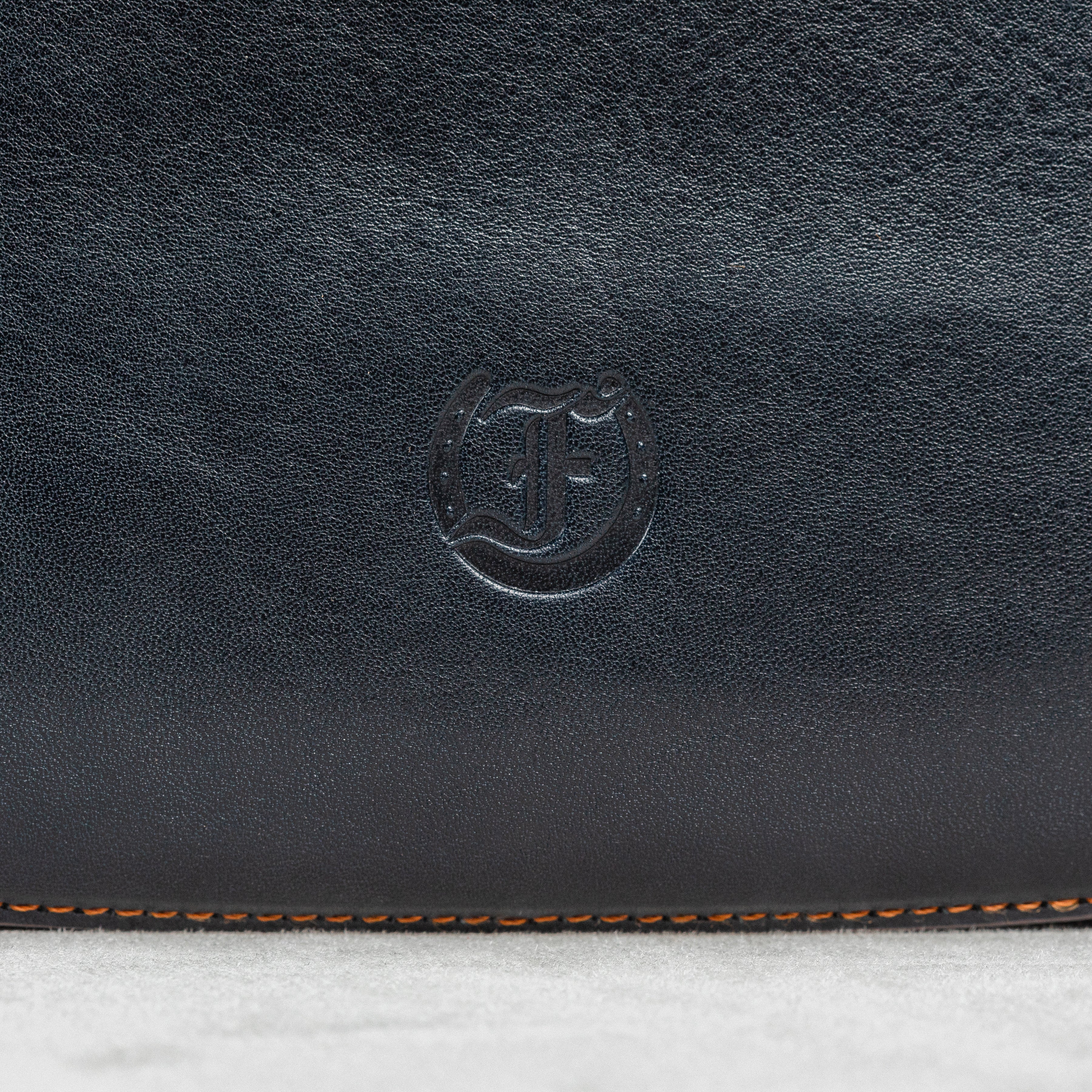 close-up of Freedman's Logo on Dark Navy Leather Murphy Bag with Orange Stitching