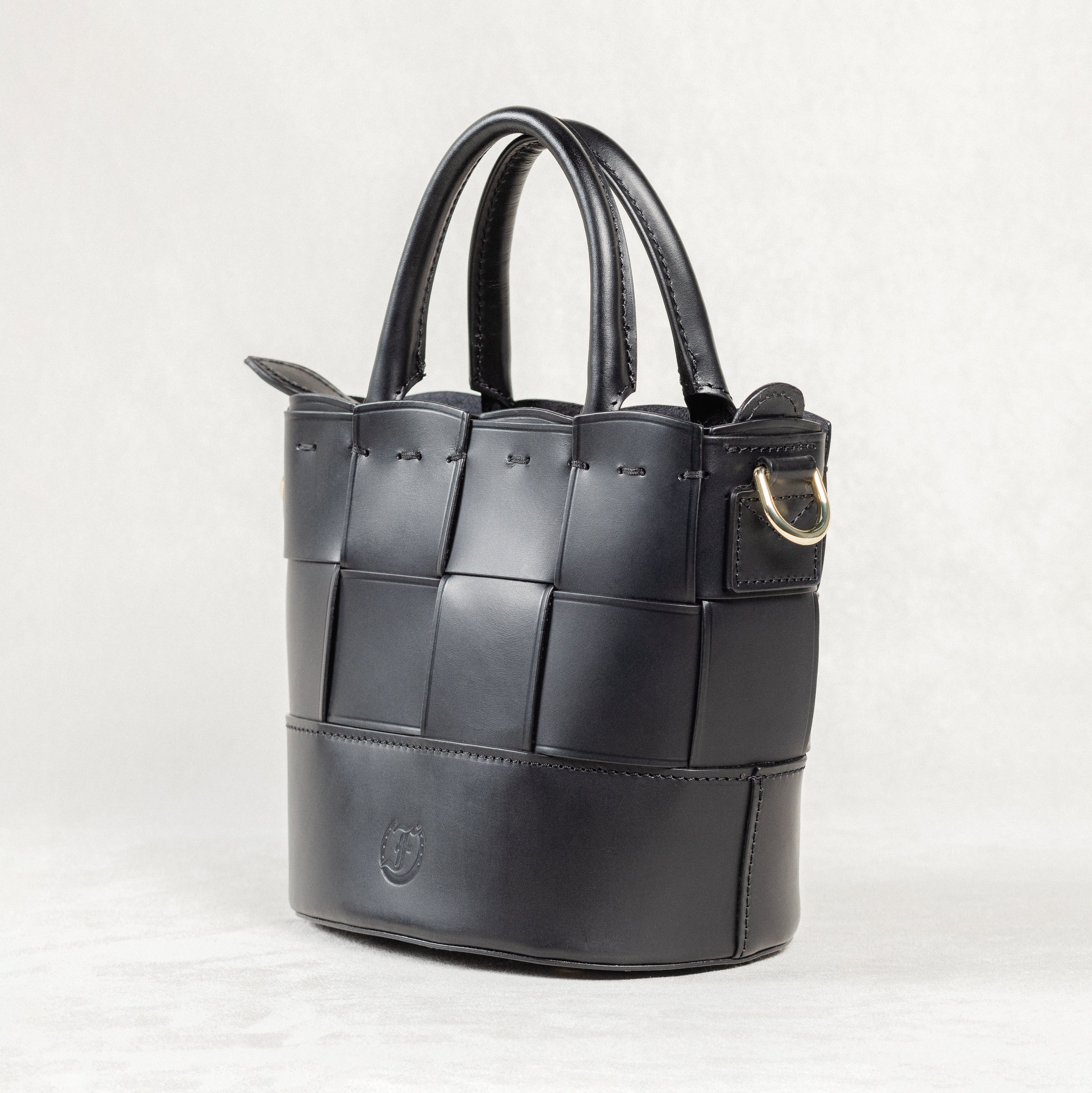 Angled view of black leather Milord Bag by Freedman's, showing woven design, structured handles, and gold-tone hardware.