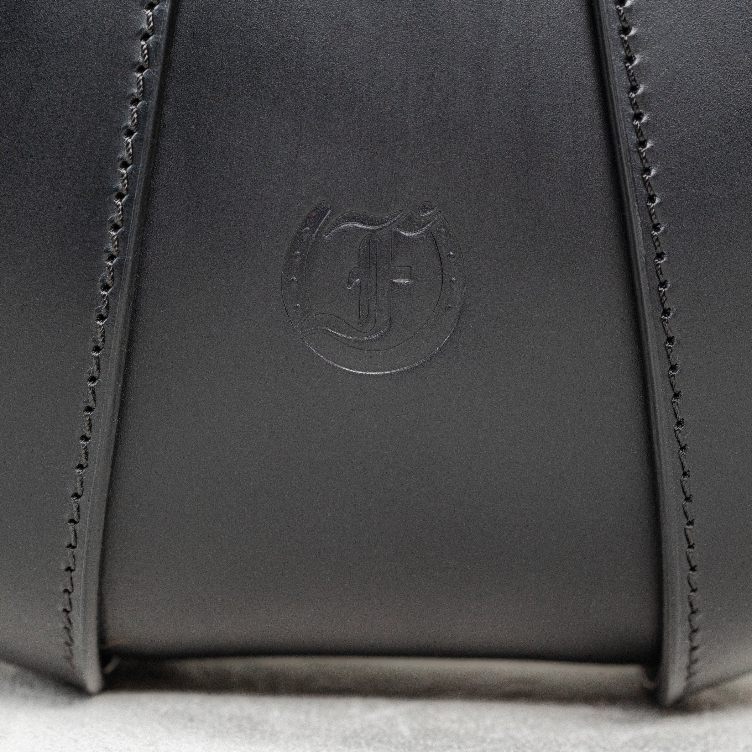 Close-up of black leather Moray Bag by Freedman's, highlighting embossed brand logo and detailed stitching.