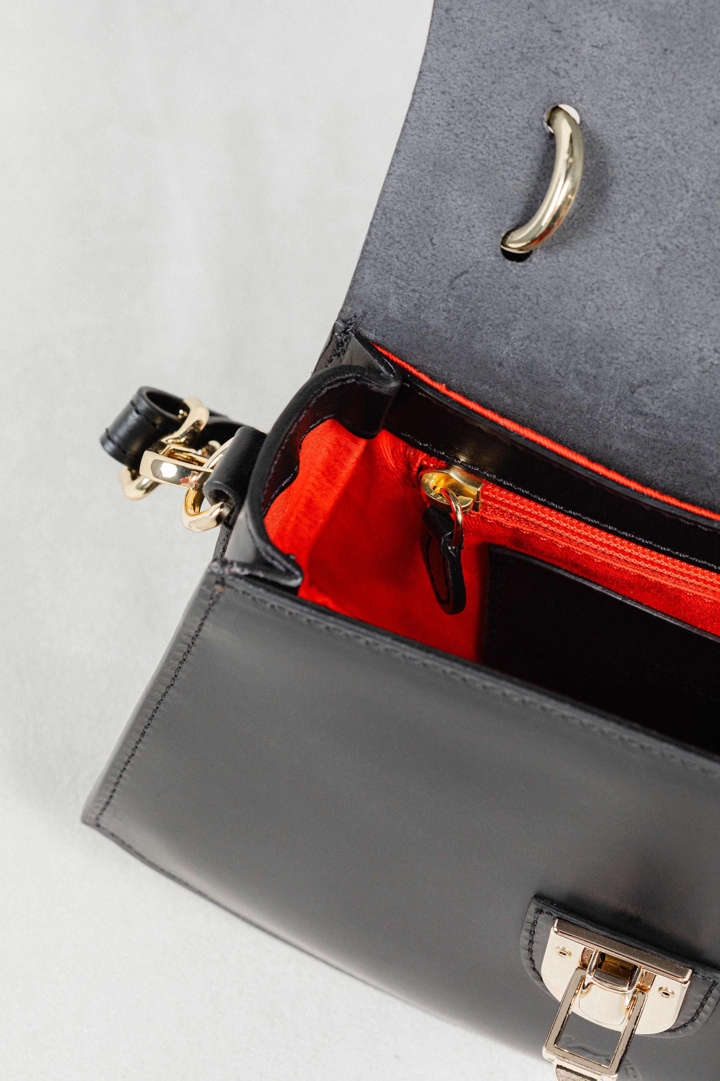 Close-up of black leather Minibus Bag by Freedman's, highlighting red interior lining, gold-tone turn-lock, and zipper.