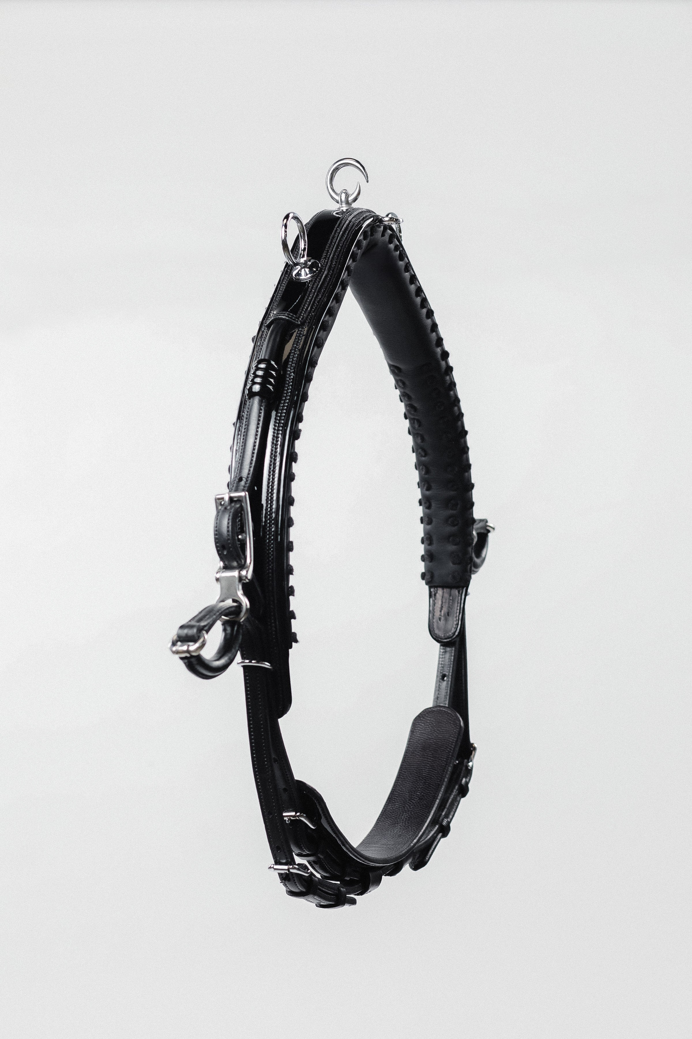 Black leather horse neck strap with silver buckles and hardware, hanging against a white background.