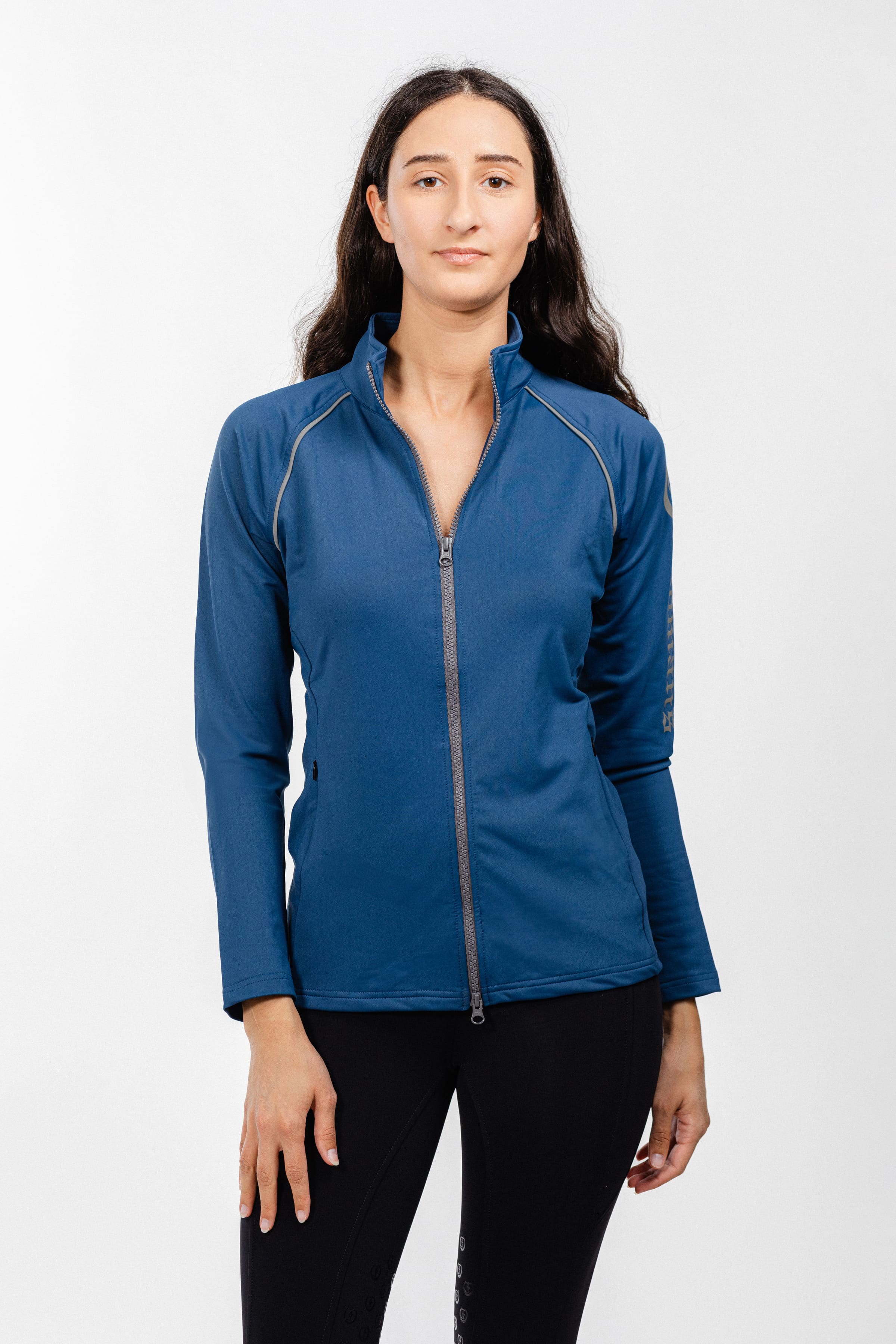 Ladies Arum Jacket by Freedman's in navy blue with silver zipper detail and reflective piping, front view on woman with long dark hair against white background, styled with black athletic pants, showcasing athletic apparel fit
