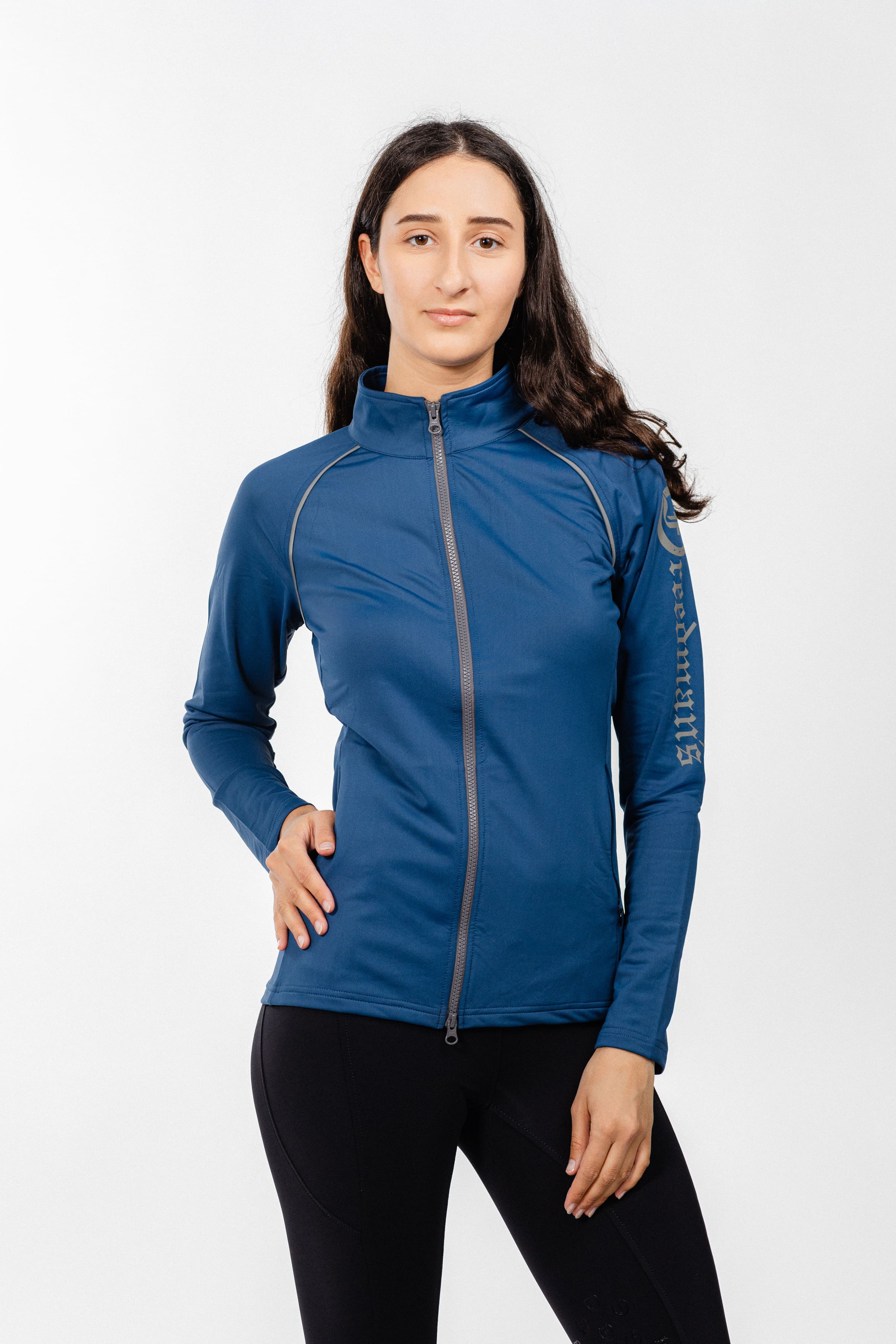 "Ladies Arum Jacket by Freedman's in navy blue with silver zipper detail and reflective piping, front view on woman with long dark hair against white background, styled with black athletic pants, showcasing athletic apparel fit"
