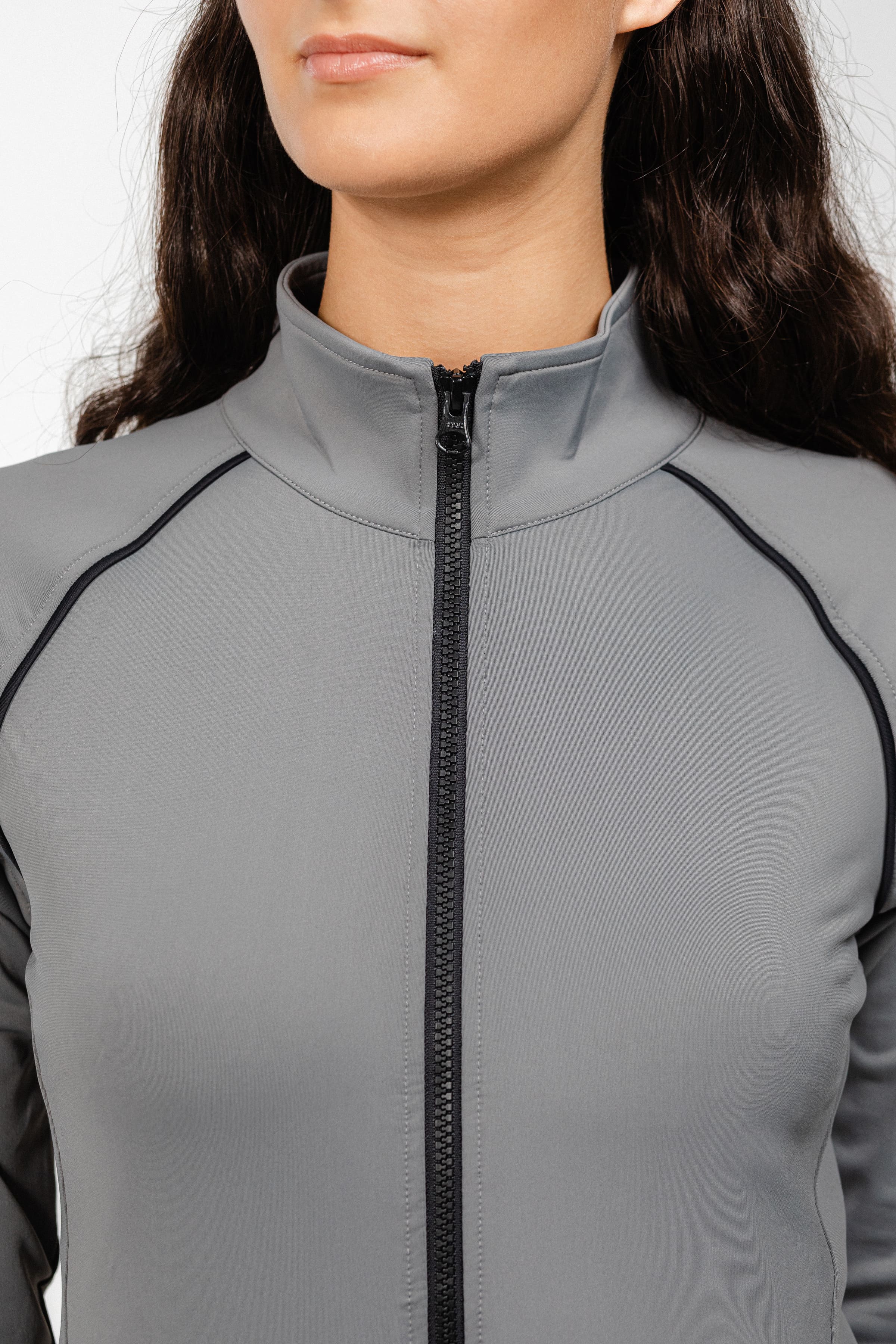 Close-up detail of Ladies Arum Jacket by Freedman's in gray, showing high collar design, black zipper, and contrast piping construction, highlighting quality stitching and fabric texture on woman with dark hair against white background