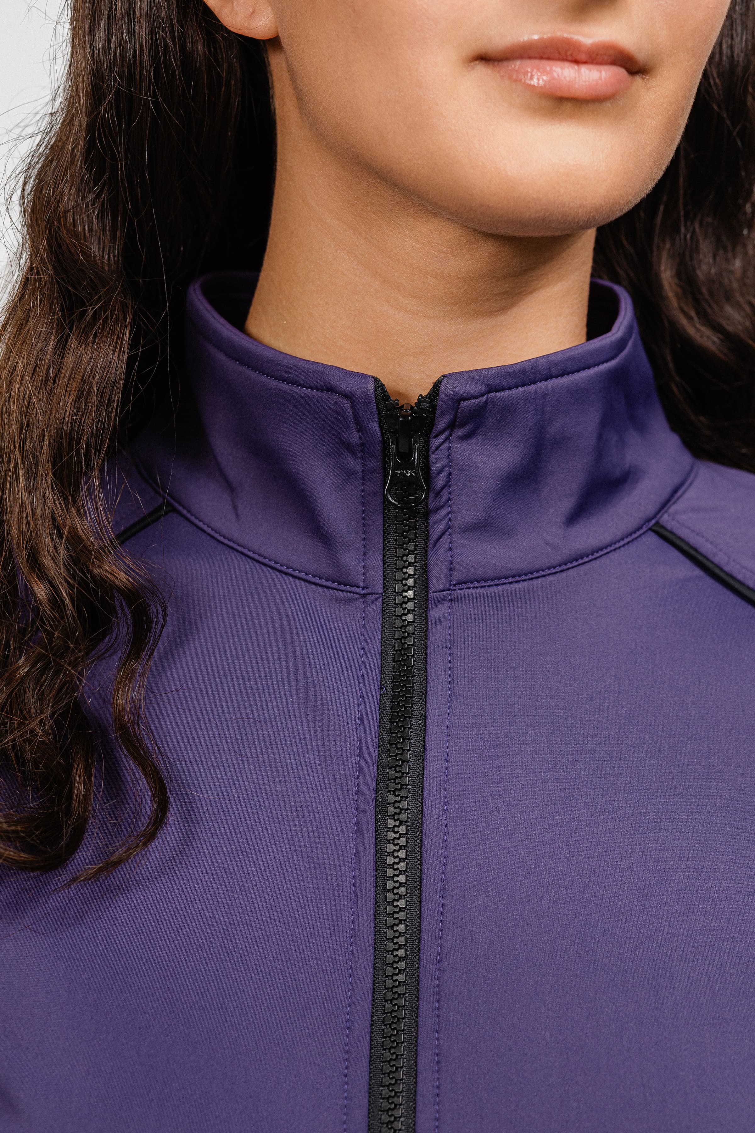 Close-up detail of Ladies Arum Jacket by Freedman's in purple, showing high collar design, black zipper, and contrast piping construction, highlighting quality stitching and fabric texture on woman with dark hair against white background