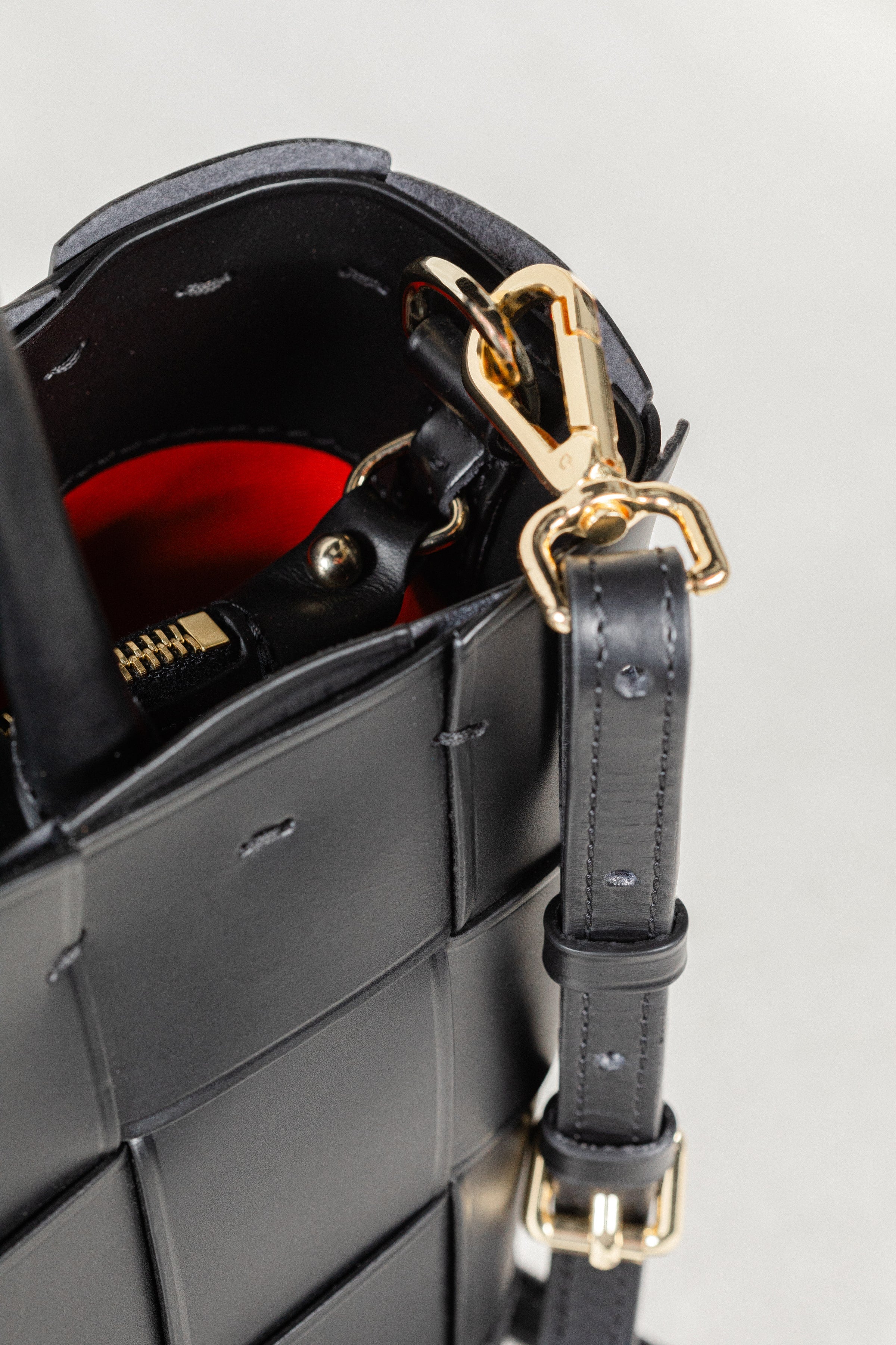 Close-up of black Manalos Bag by Freedman's, highlighting gold-tone hardware, adjustable strap, and contrasting red interior.
