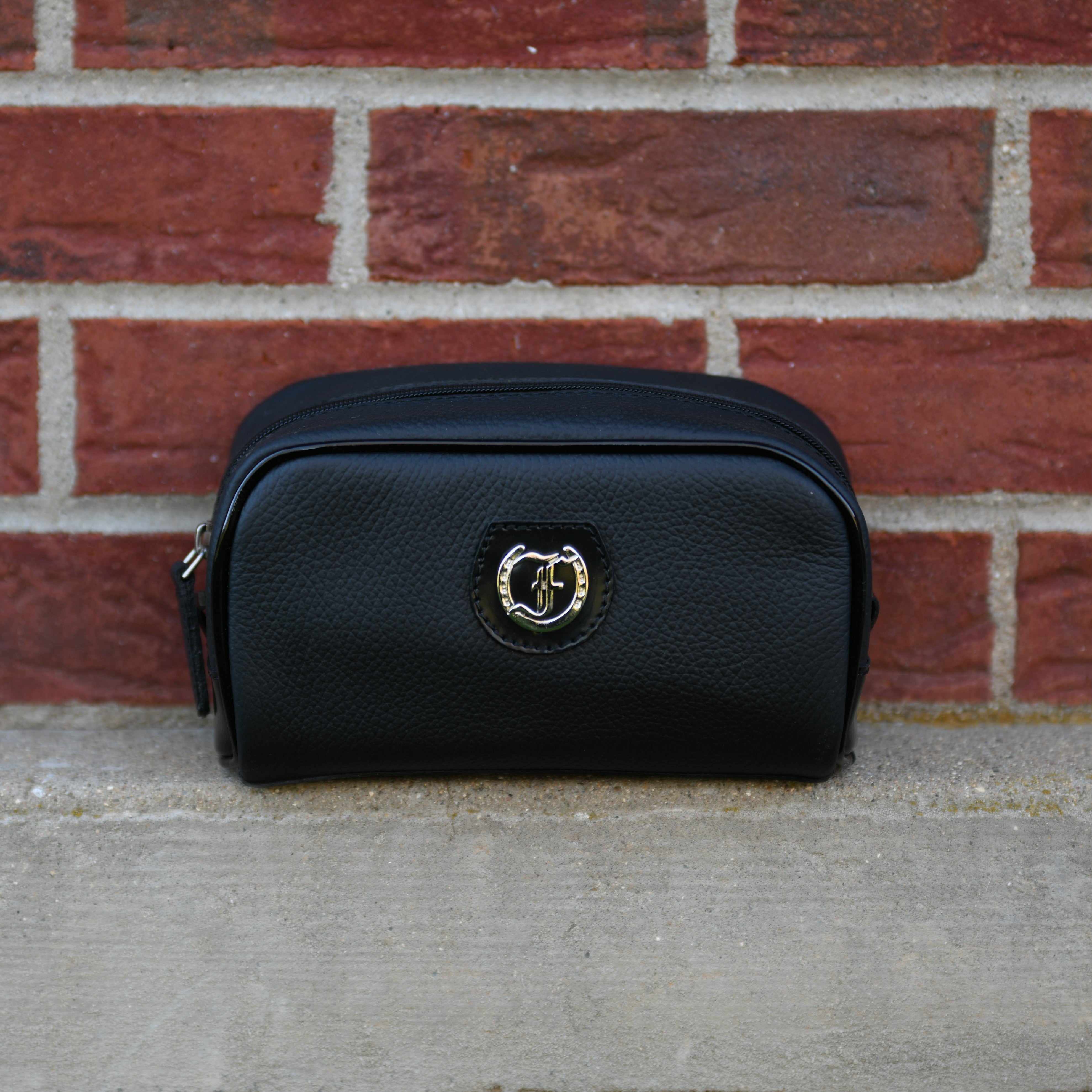 Freedman's The Viceroy - Ladies Essentials Pouch, black leather, embossed "F" logo on front, side handle, outdoor setting with brick and wood background.