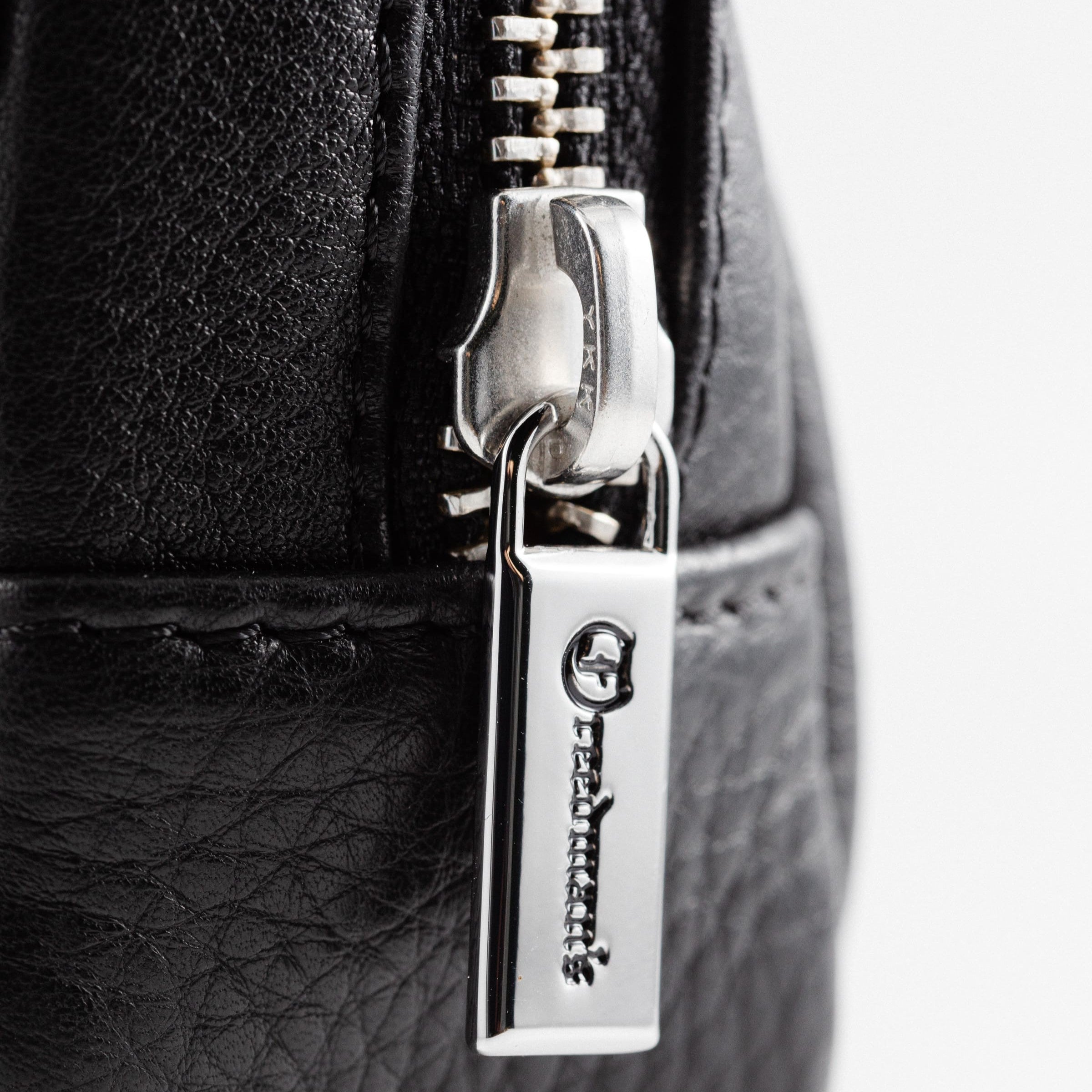 Extreme close-up of Freedman's Norfolk Crossbody Bag in Black Leather, showing silver zipper pull with engraved Freedman's logo.