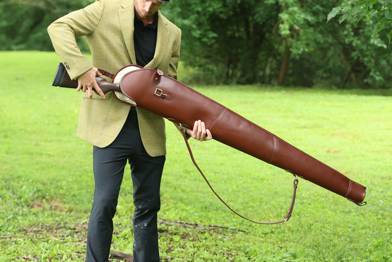A man outdoors holding a Havana brown leather Sandringham Gun Slip, crafted by Freedman’s Harness.
