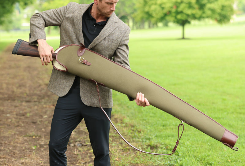 A man outdoors holding a Military Green Sandringham Gun Slip with Havana brown leather accents, crafted by Freedman’s Harness.