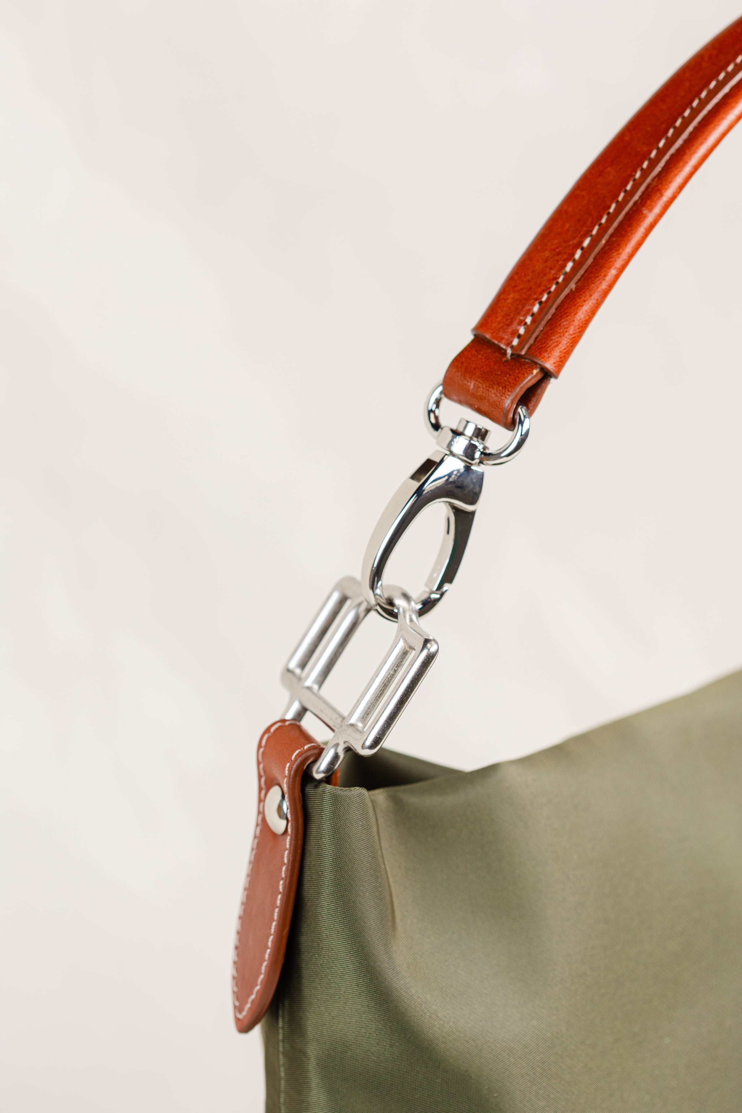 Travois Bag by Freedman's, close-up shot of the silver metal clasp and brown leather strap on the olive green bag, showing fine detail and stitching.
