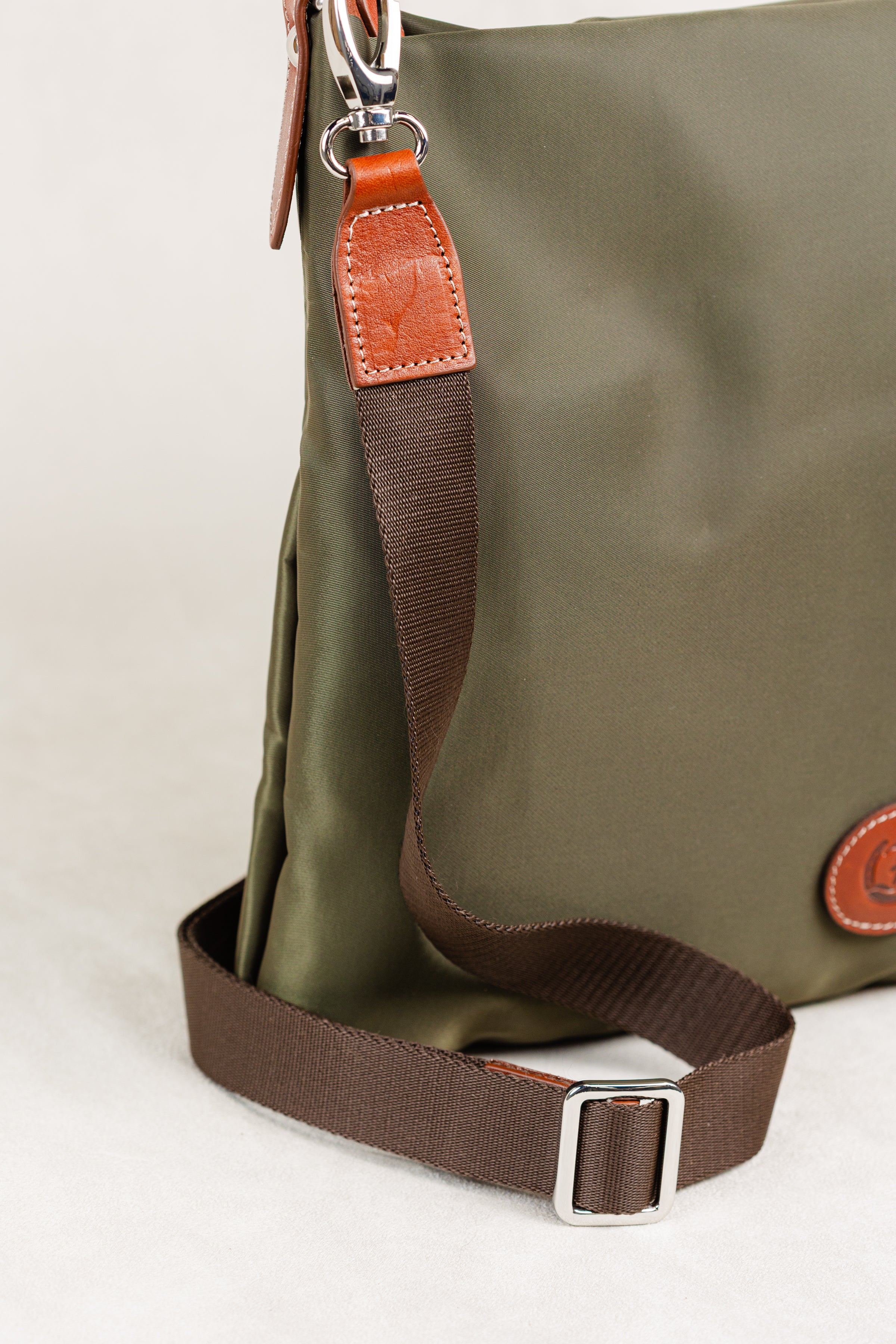 Freedman's Travois Bag in olive green, detailed view of the brown fabric strap, leather attachment with stitching, and silver adjustable buckle.