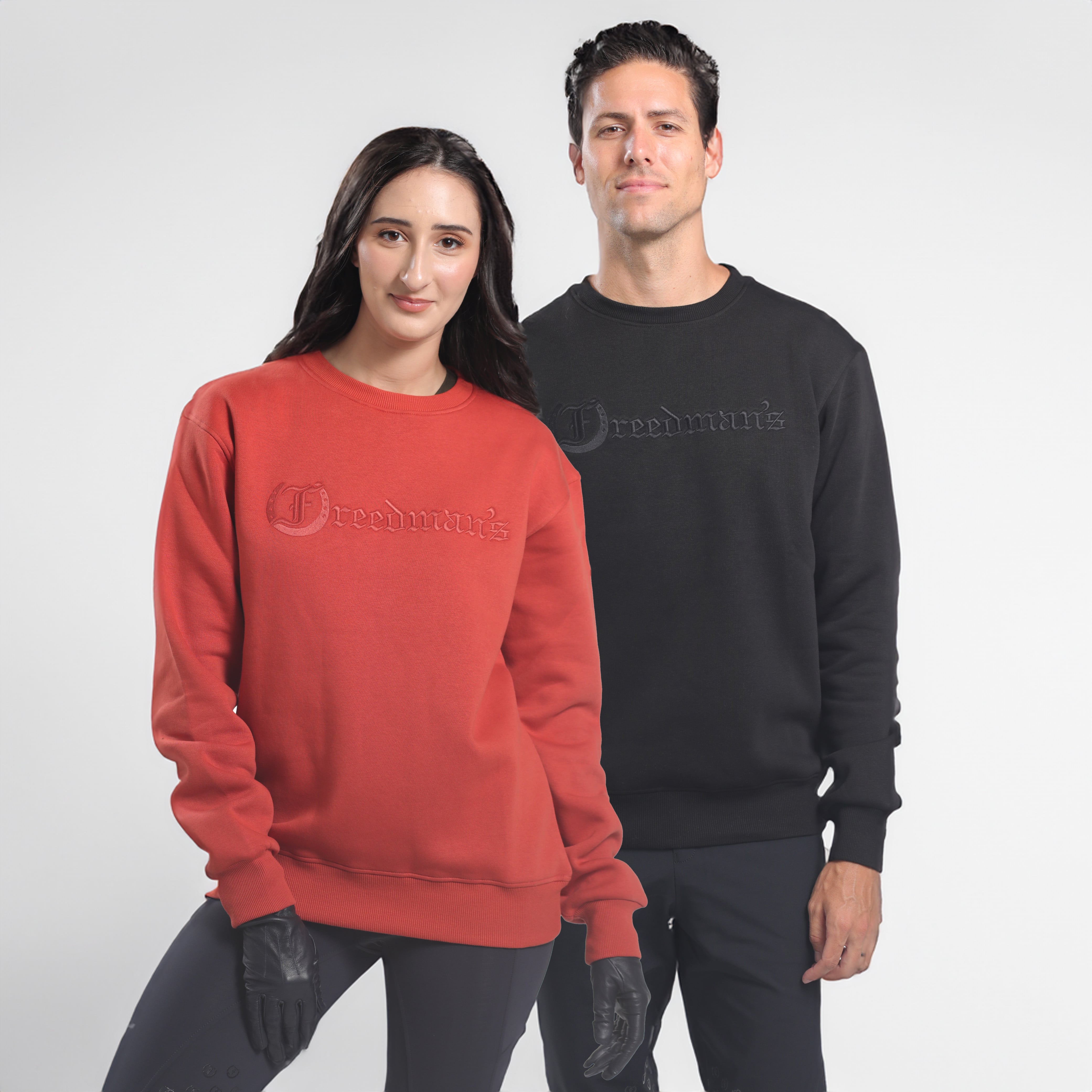 Man and woman wearing Freedman's embroidered crewneck sweatshirts in black and Brick Red. These stylish and cozy sweatshirts feature a tonal Freedman’s logo, perfect for casual wear and layering