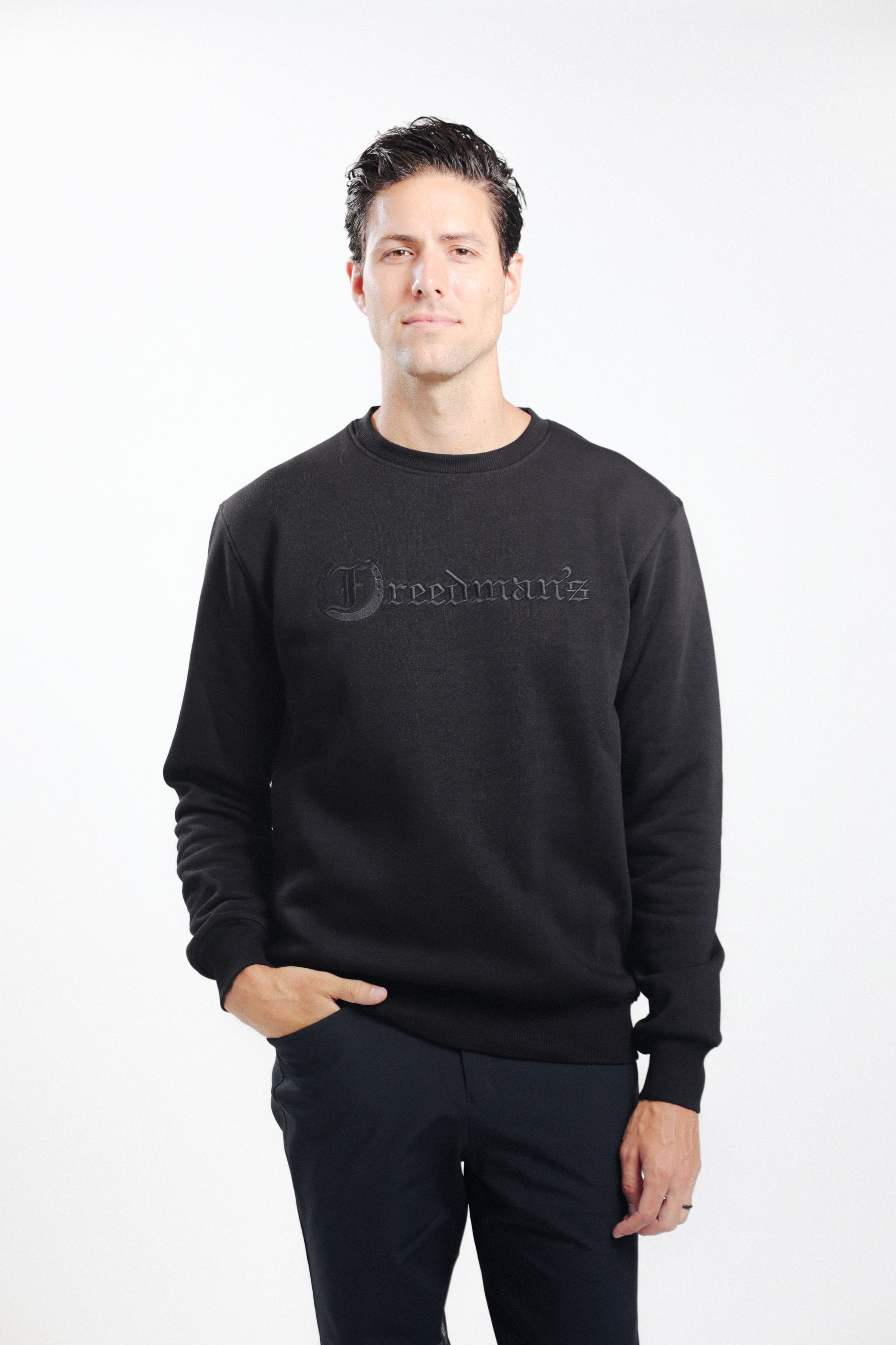 Man wearing Freedman's embroidered crewneck sweatshirts in black. These stylish and cozy sweatshirts feature a tonal Freedman’s logo, perfect for casual wear and layering