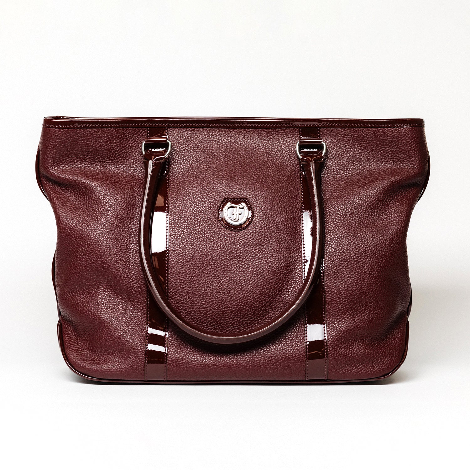 reedman's Victoria Tote, Burgundy textured leather, high gloss patent leather handles, silver circular logo on front, light contrast stitching, light background.