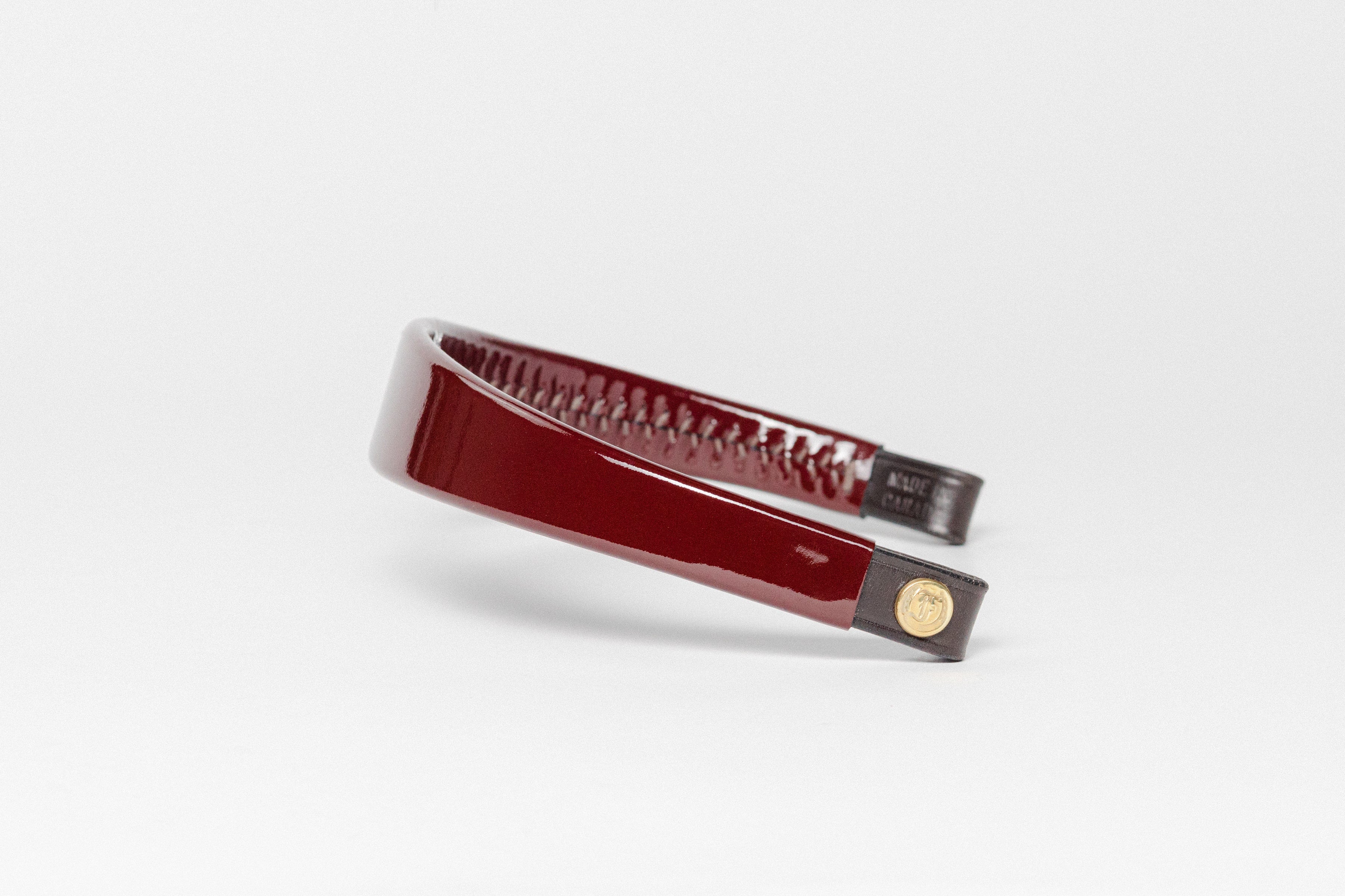 Glossy Burgundy patent leather browband, wide tapered design, dark leather ends with gold button, angled perspective.