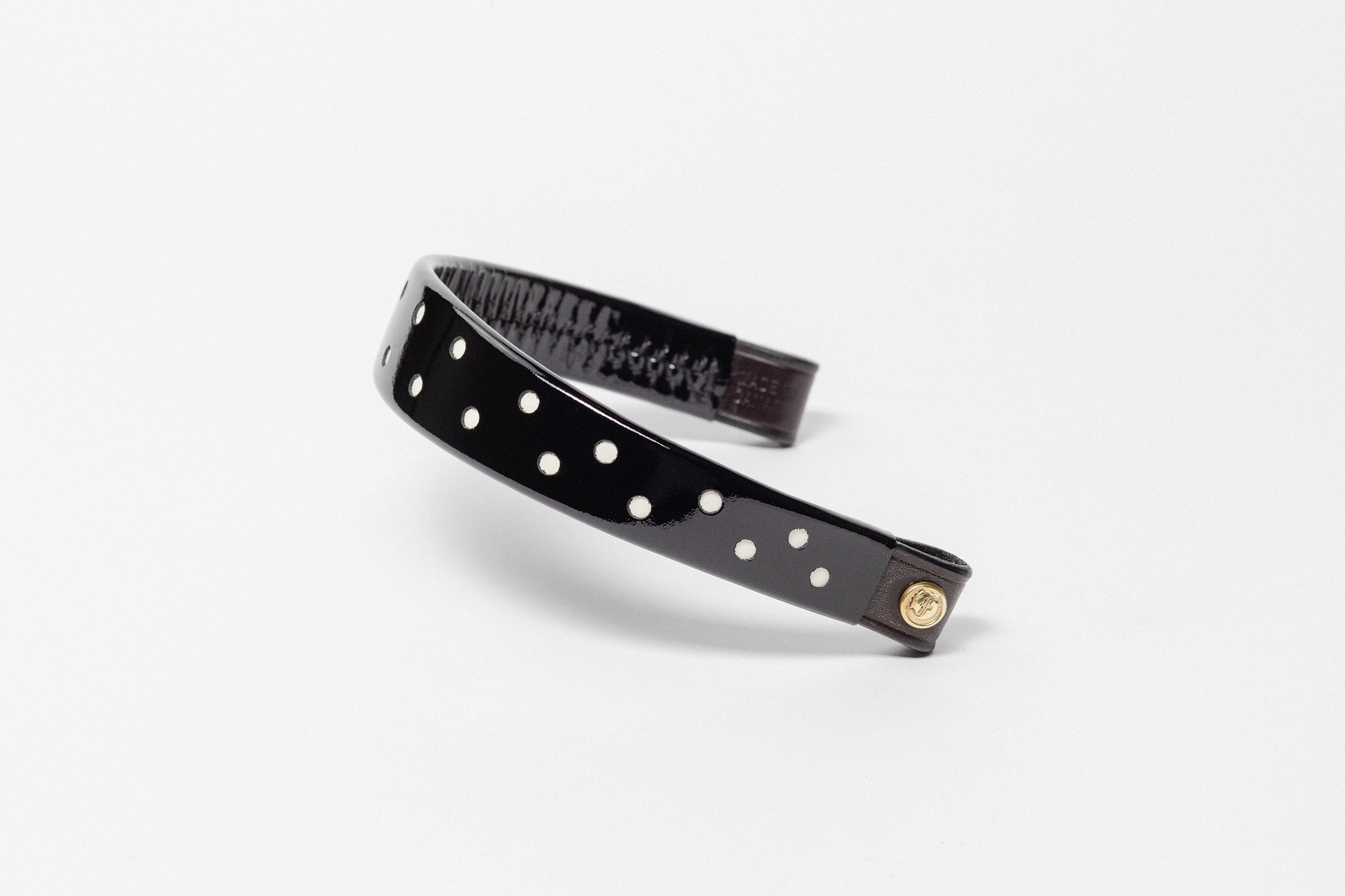 Black Patent Leather Browband with small white dots, wide tapered design, polished brass Freedman logo buttons, and dark leather ends, angled view.