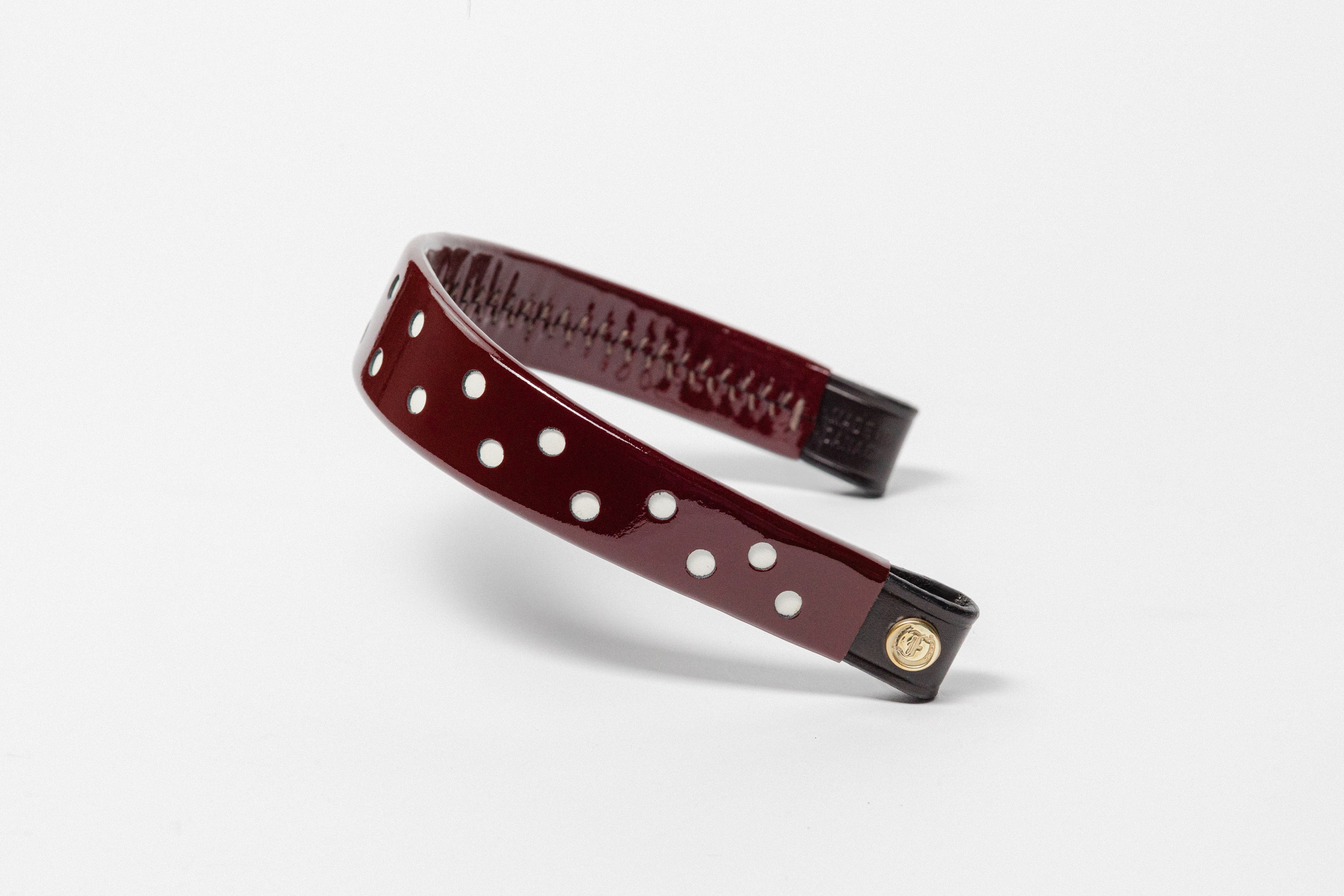 Burgundy Patent Leather Browband with white dots, wide tapered design, polished brass Freedman logo buttons, and dark leather ends, angled view.