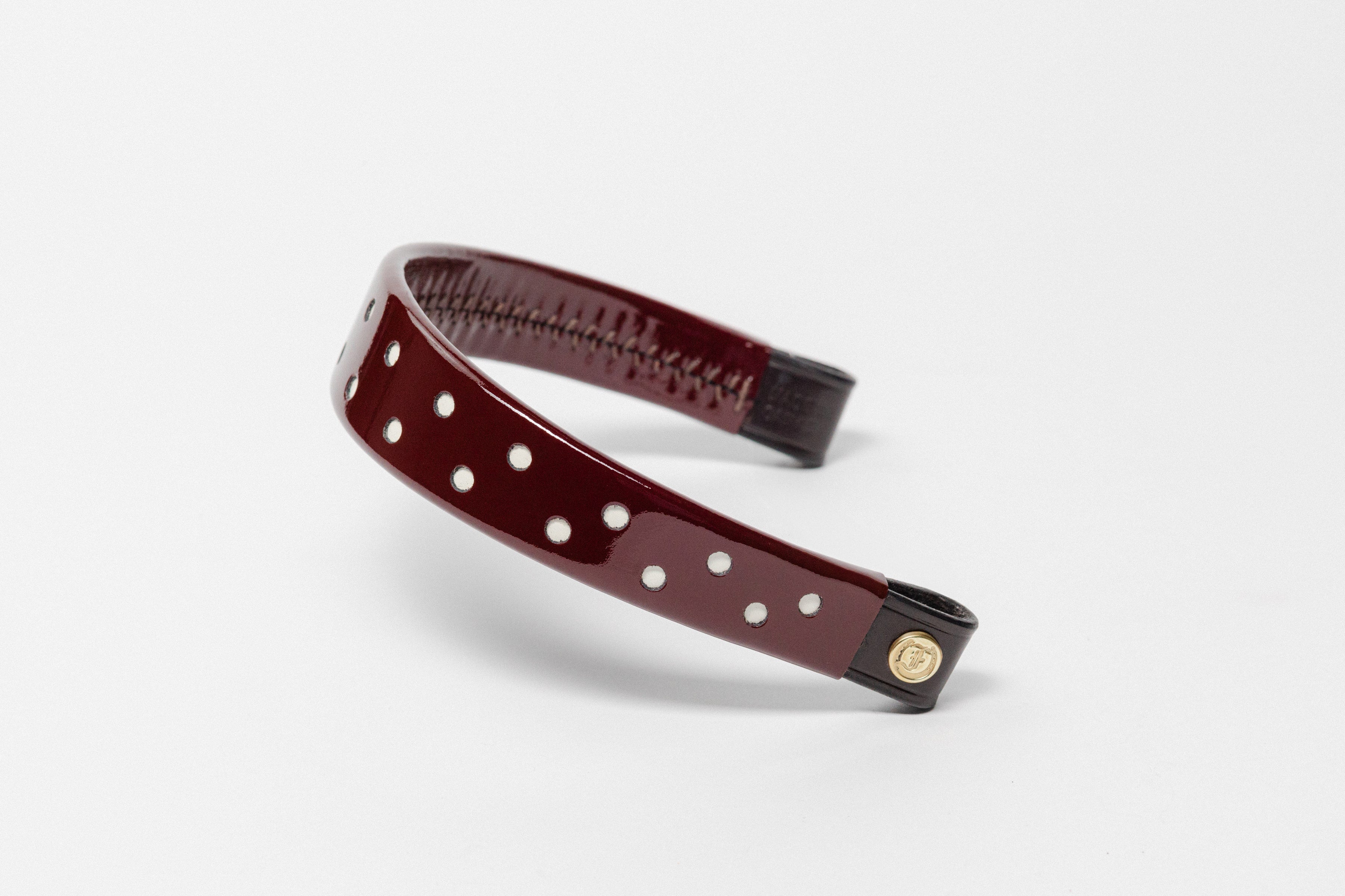 Burgundy Patent Leather Browband with small white dots, wide tapered design, polished brass Freedman logo buttons, and dark leather ends, angled view.