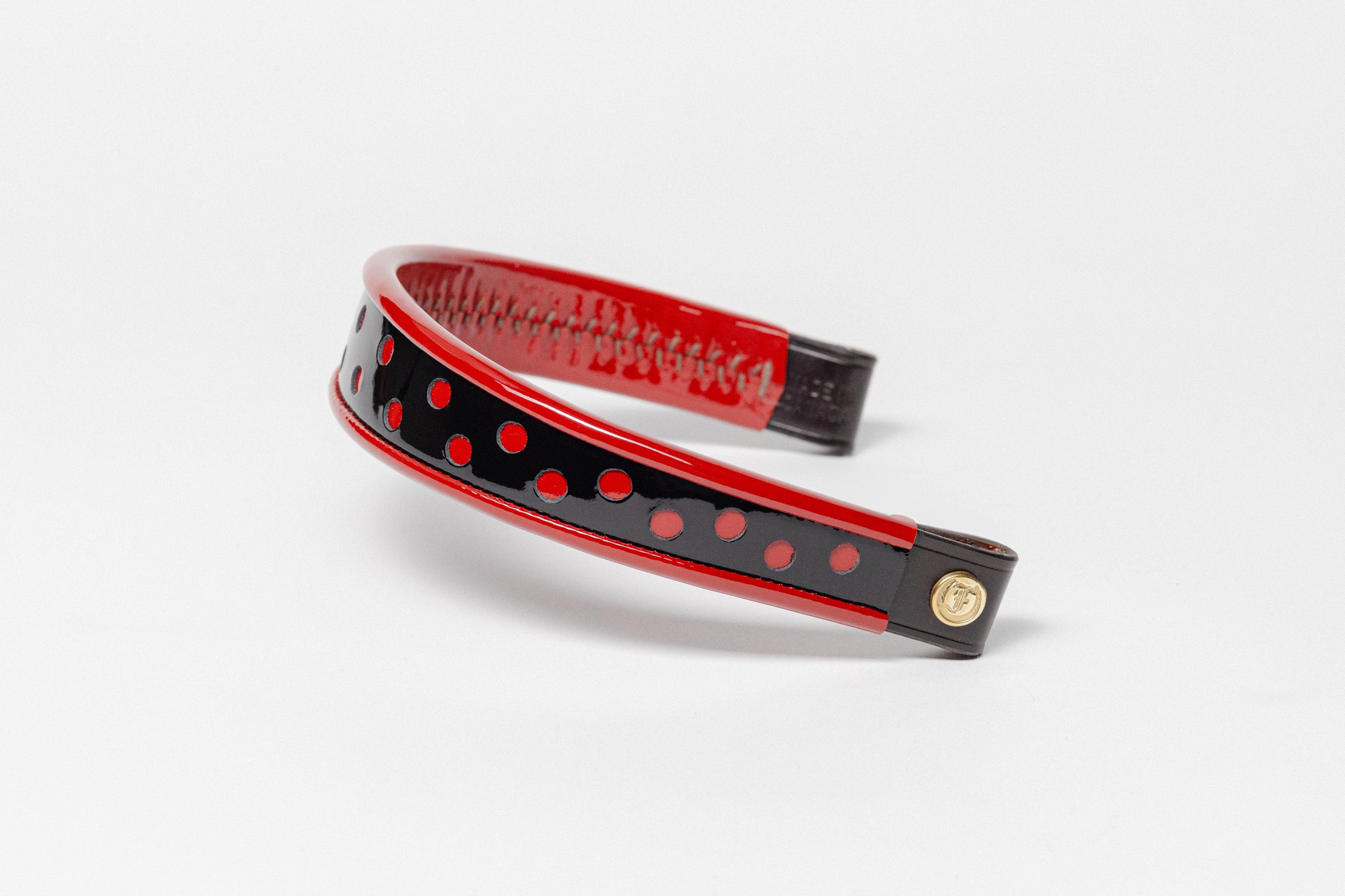 Red and white dot patent leather browband, wide tapered design, turned edge, dark leather ends with gold button, shown angled .