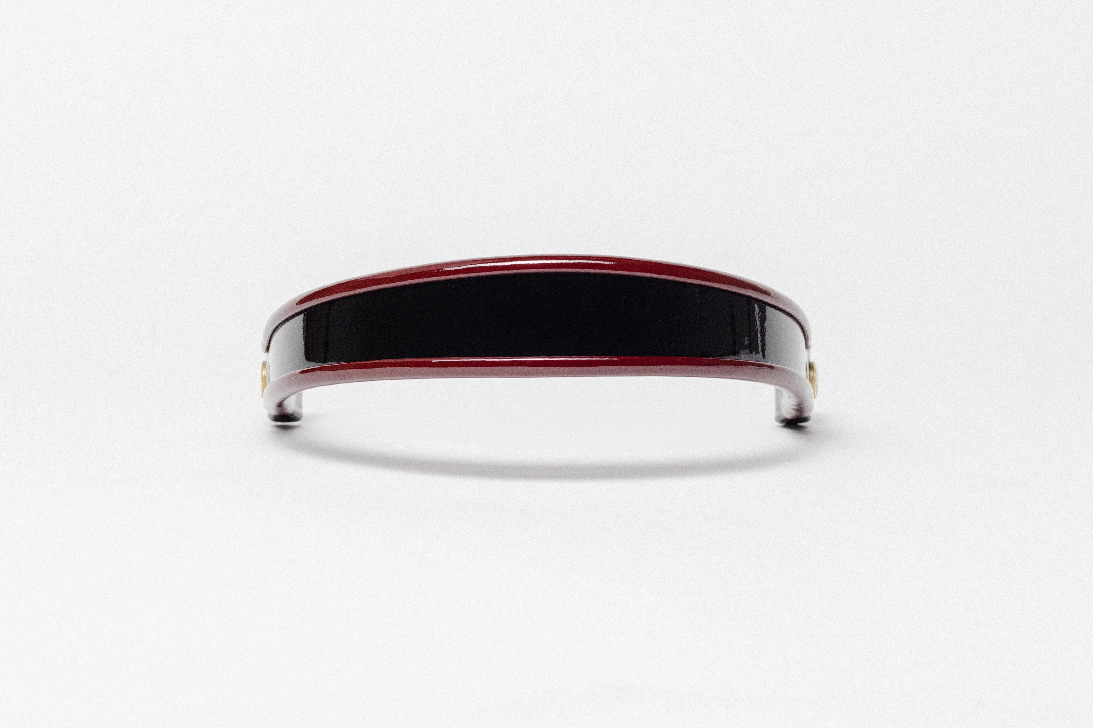 Red and black patent leather browband, wide tapered design, turned edge, polished brass Freedman logo buttons, frontal view.