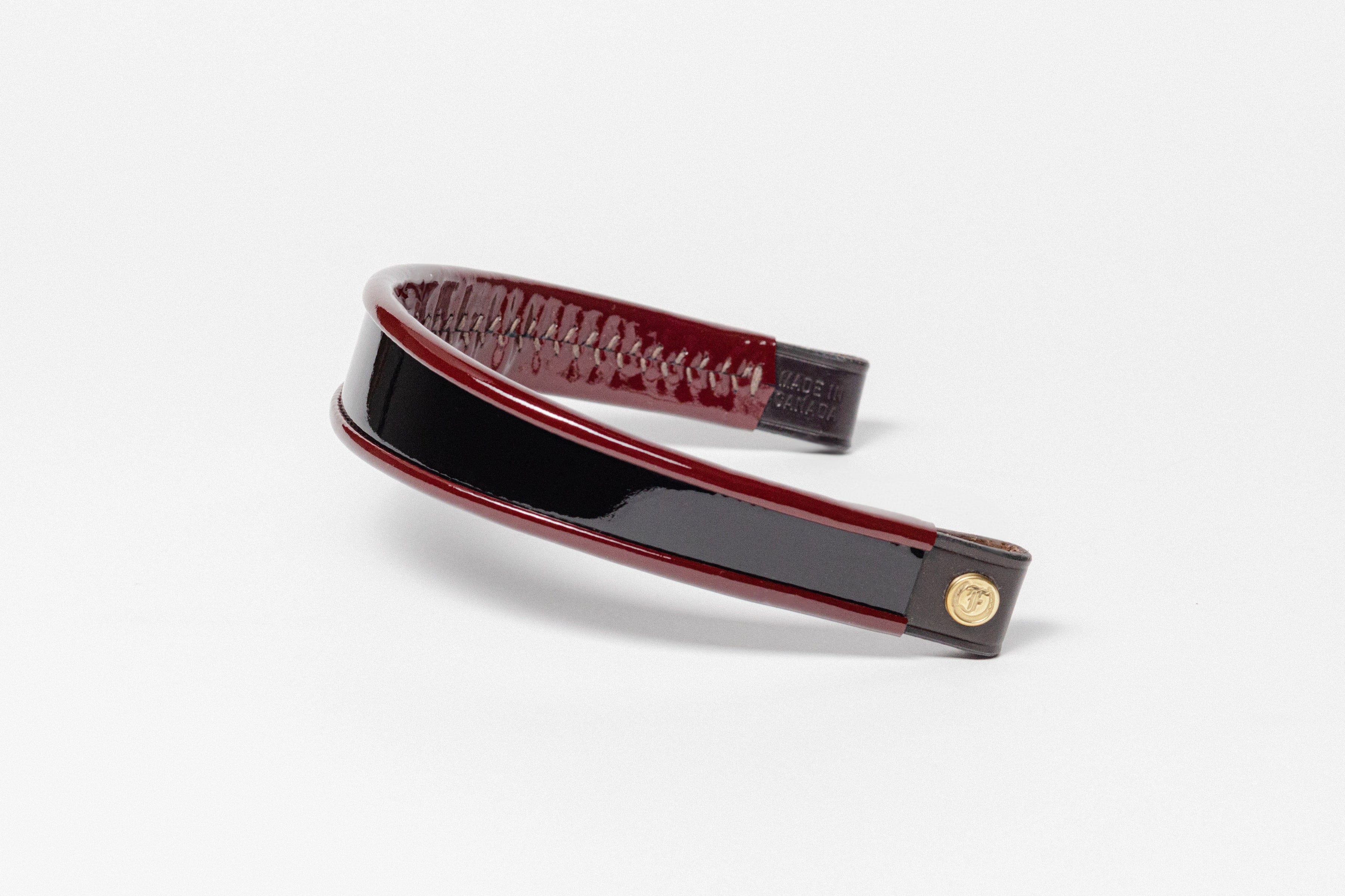Burgundy and black paten leather browband, wide tapered design, turned edge, polished brass Freedman logo buttons, angled perspective.