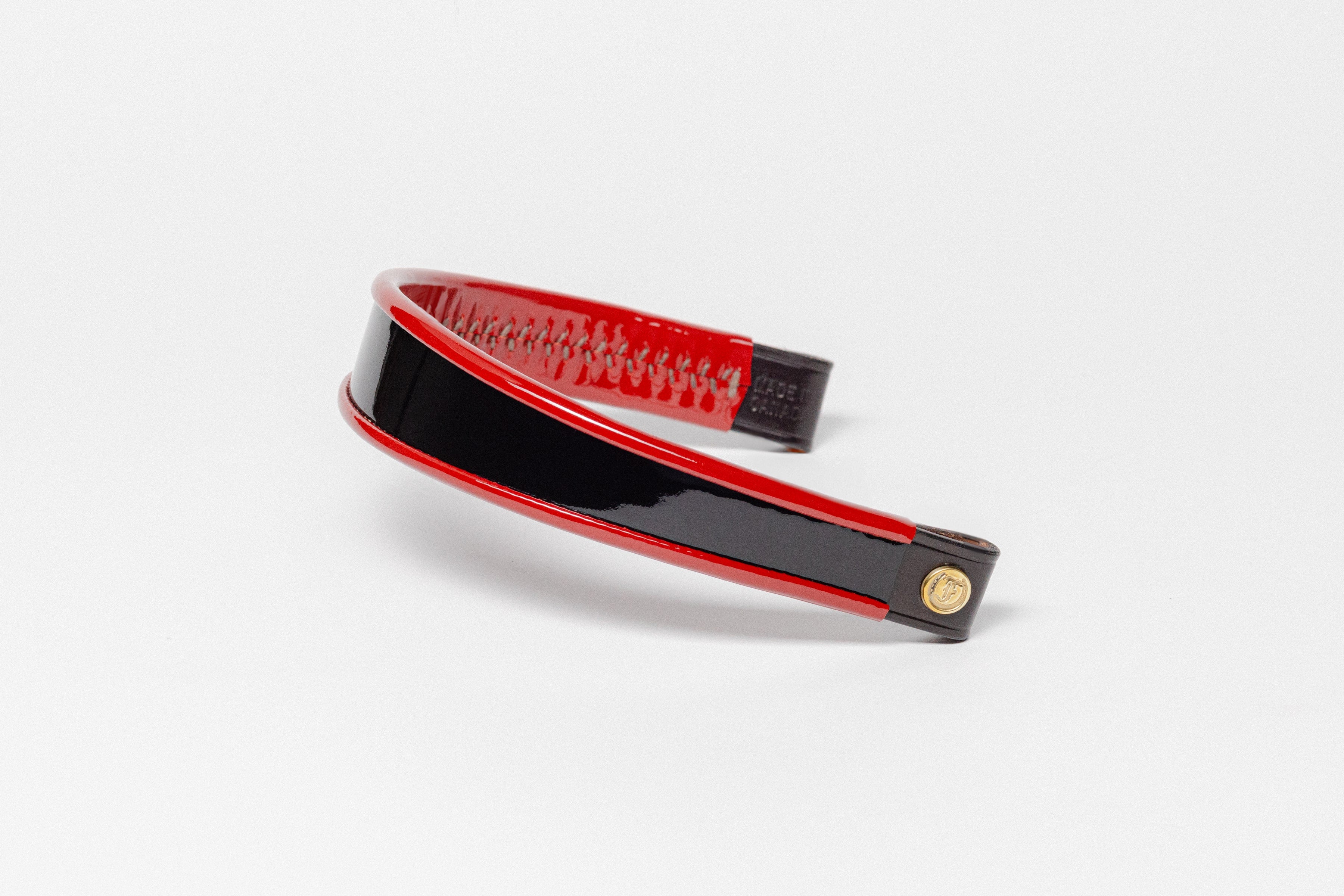 Red and black patent leather browband, wide tapered design, turned edge, polished brass Freedman logo buttons, and dark leather ends, angled view.