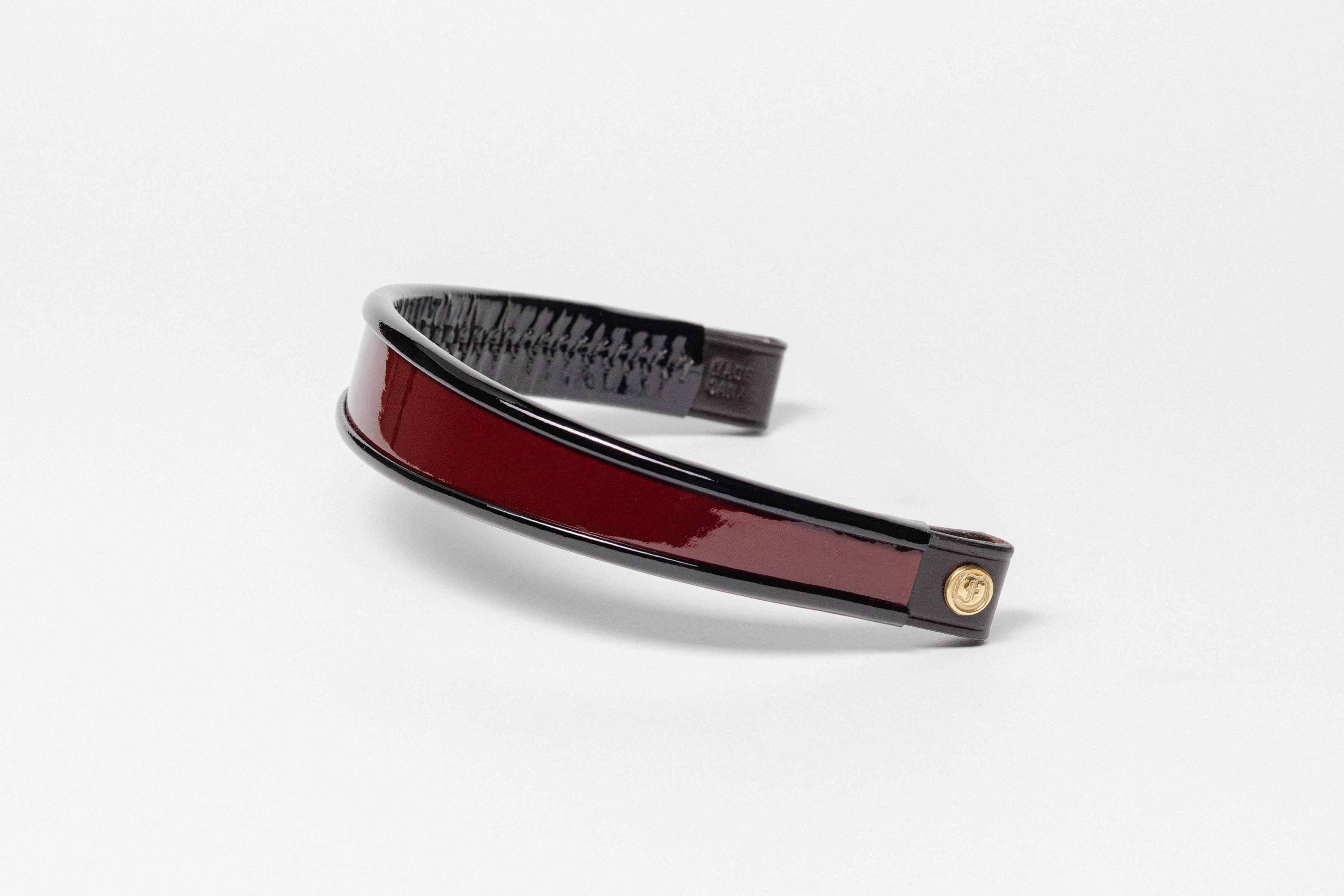 Burgundy and black patent leather browband, wide tapered design, polished brass Freedman logo buttons, and dark leather ends, angled view.