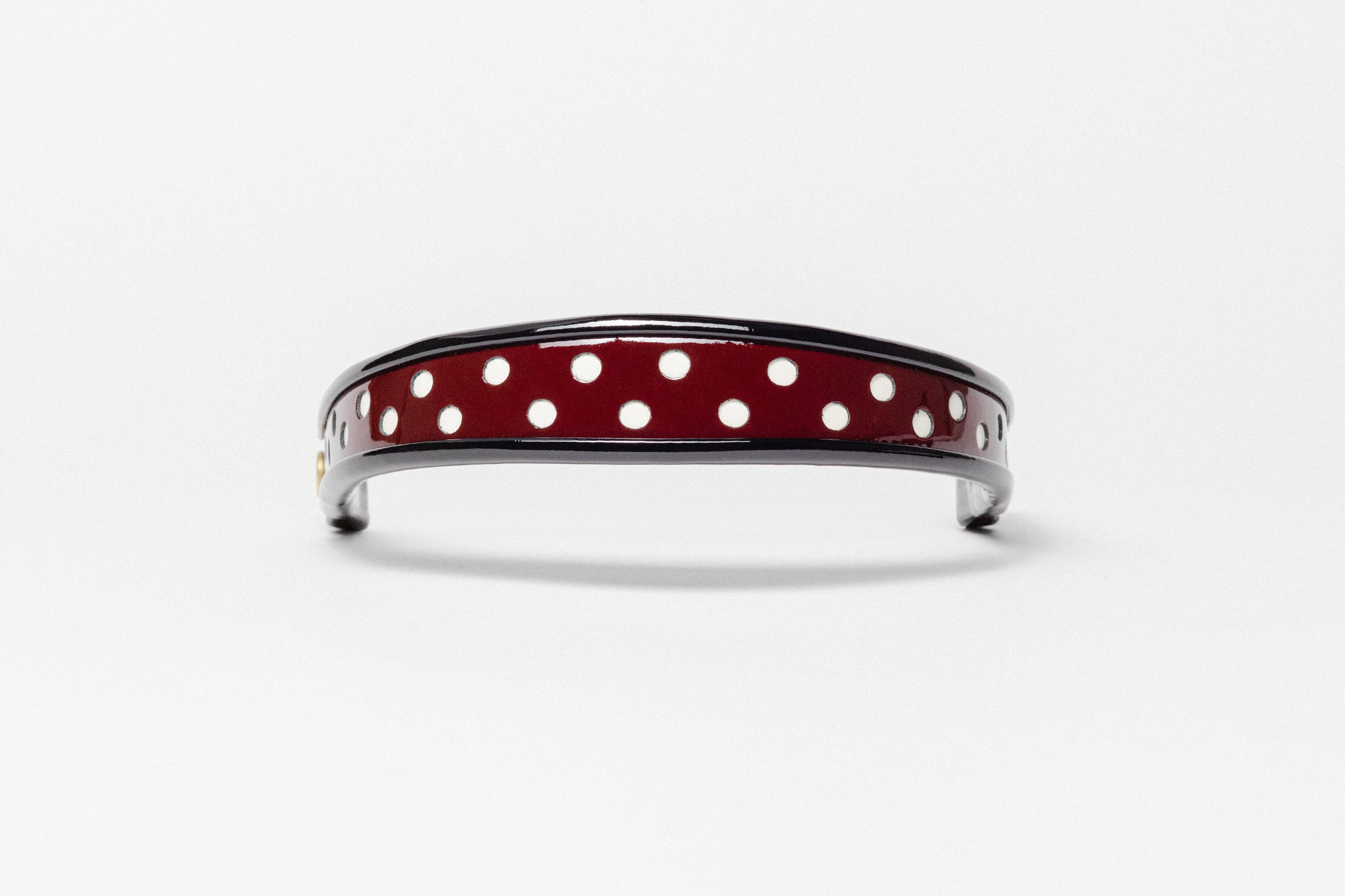 Burgundy and white dot patent leather browband, wide tapered design, turned edge, dark leather ends with gold button, shown flat.