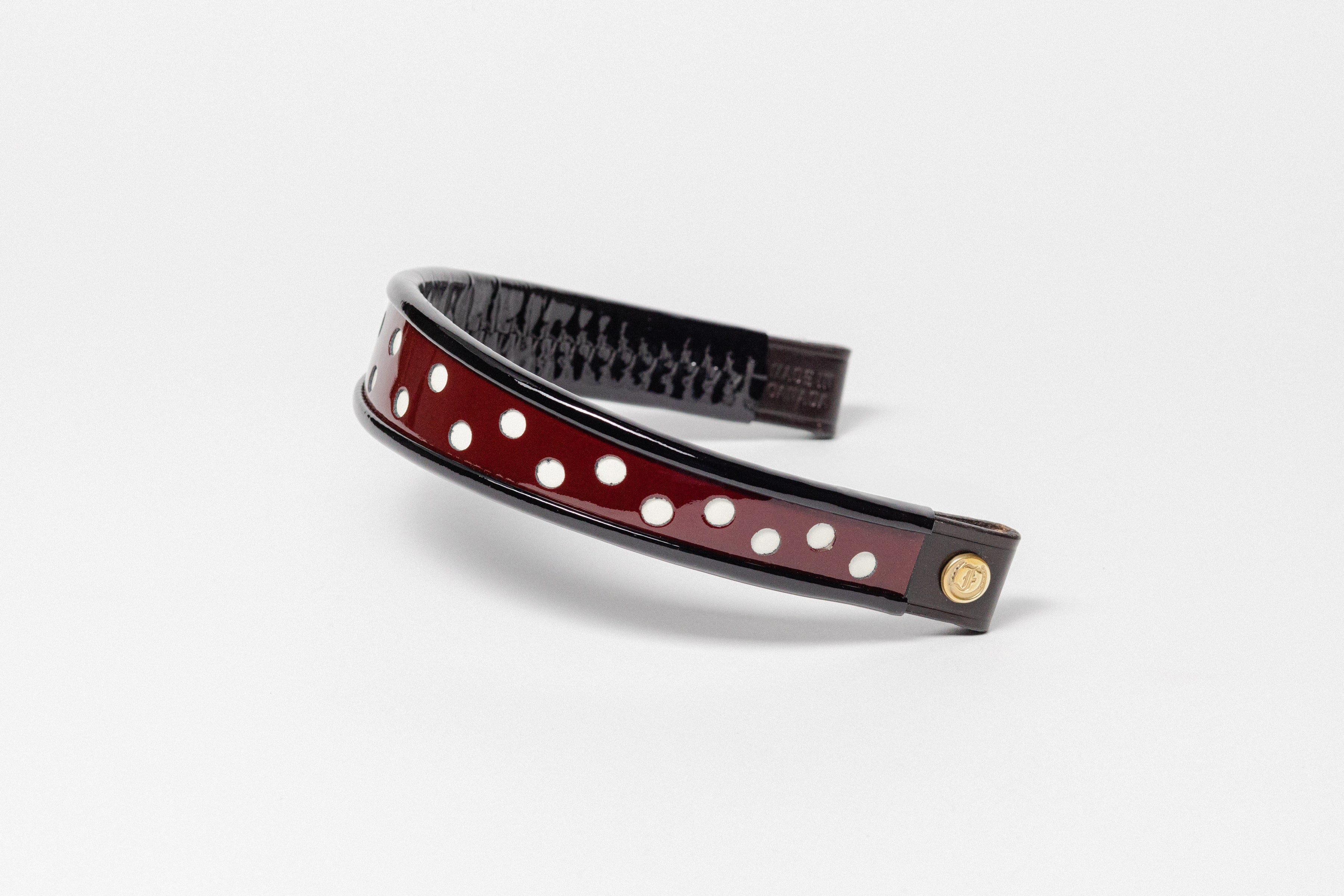 Burgundy and white dot patent leather browband, wide tapered design, turned edge, dark leather ends with gold button, shown flat.