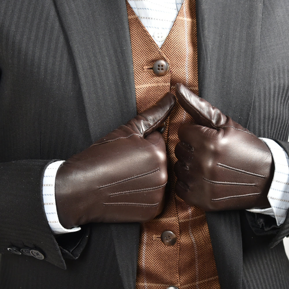 The Yorkville Show Glove, dark brown leather, worn on both hands with thumbs up gesture, dark suit jacket with striped vest and shirt visible, light background.