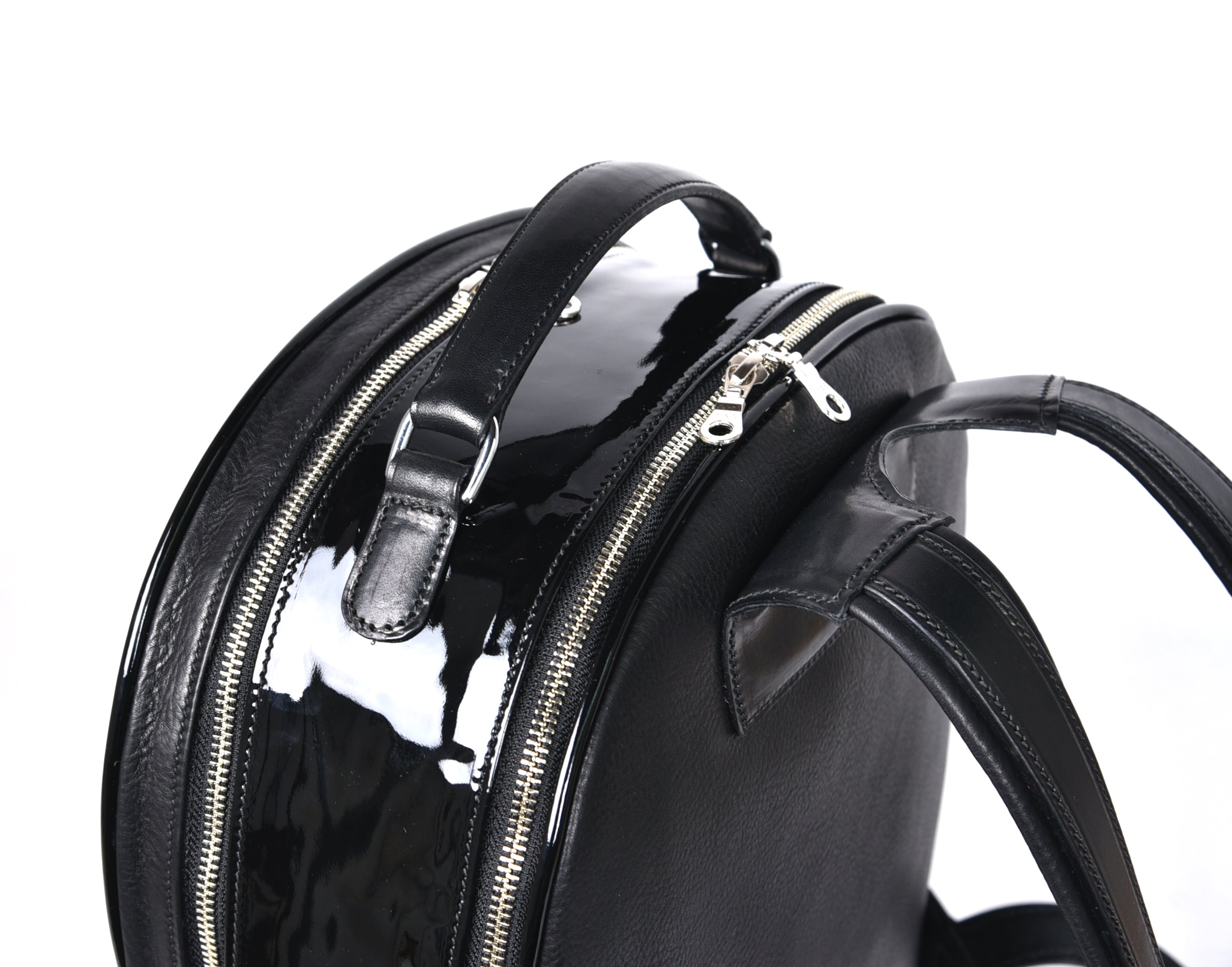 Close-up of black leather backpack, The Jaunty by Freedman's, showing zipper pulls, top handle, and patent leather accent.